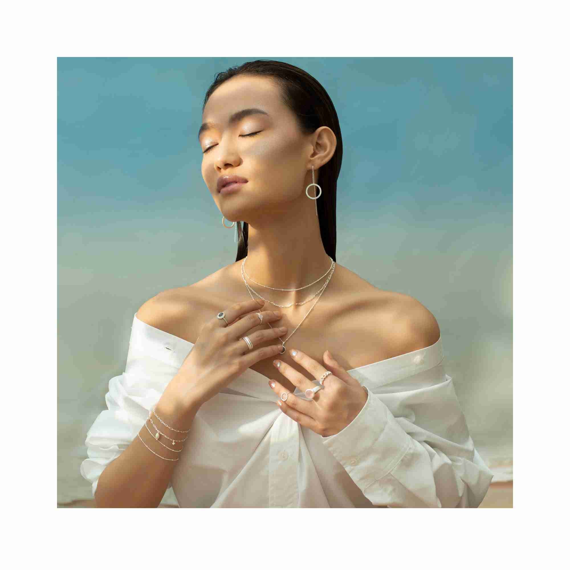 Close-up lifestyle shot of silver Shimmering Disks chain threader earrings resting on draped white linen, showcasing the signature hand-brushed matte texture and delicate circular disks — Protsaah Zurich.