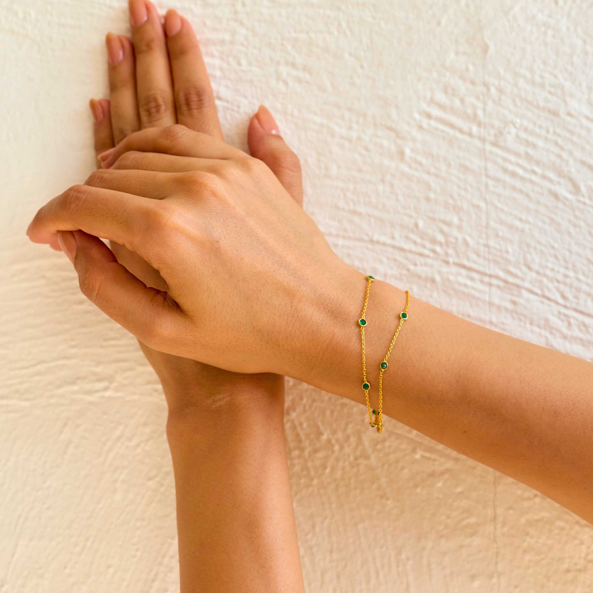 A close-up lifestyle shot of a person's wrist wearing the Dew Drops Green Onyx Studded Chain Bracelet Gold, showcasing the delicate double gold chains and bezel-set green onyx gemstones under warm, natural sunlight.
