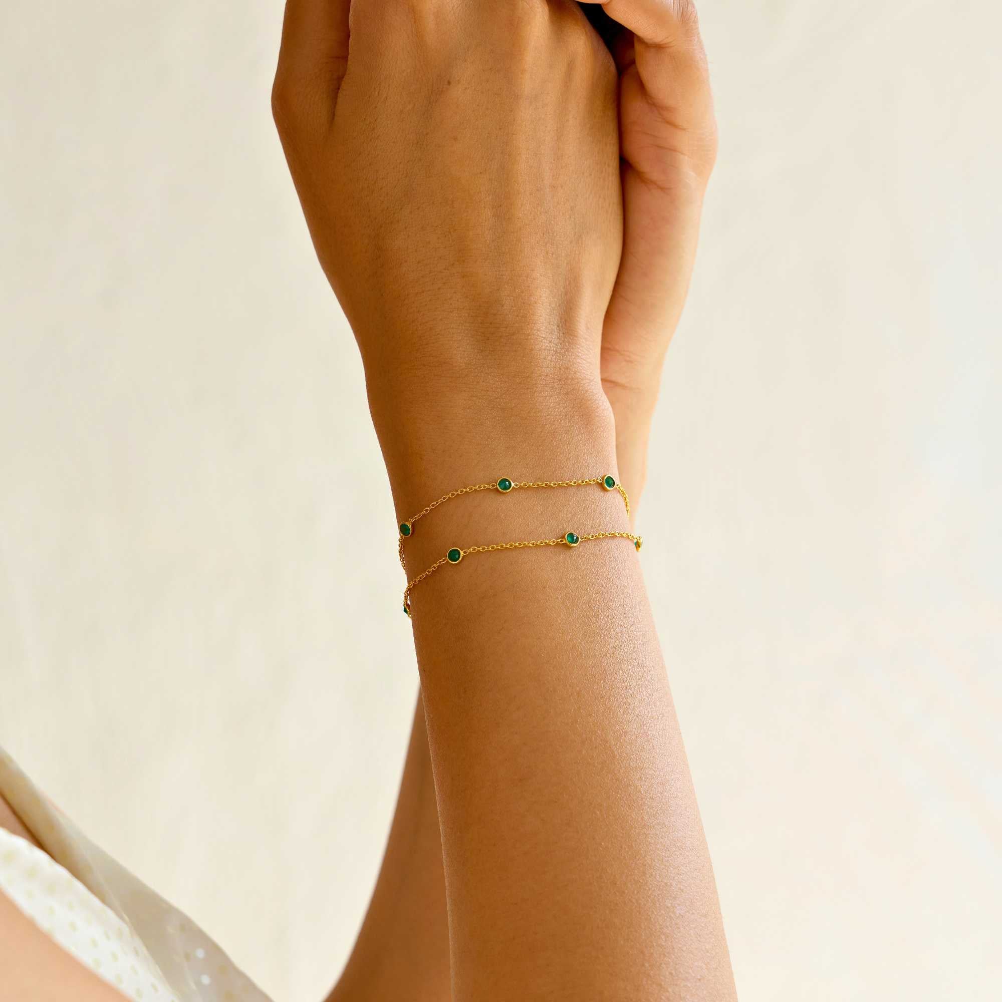 A close-up lifestyle shot of a person's wrist wearing the Dew Drops Green Onyx Studded Chain Bracelet Gold, showcasing the delicate double gold chains and bezel-set green onyx gemstones under warm, natural sunlight.