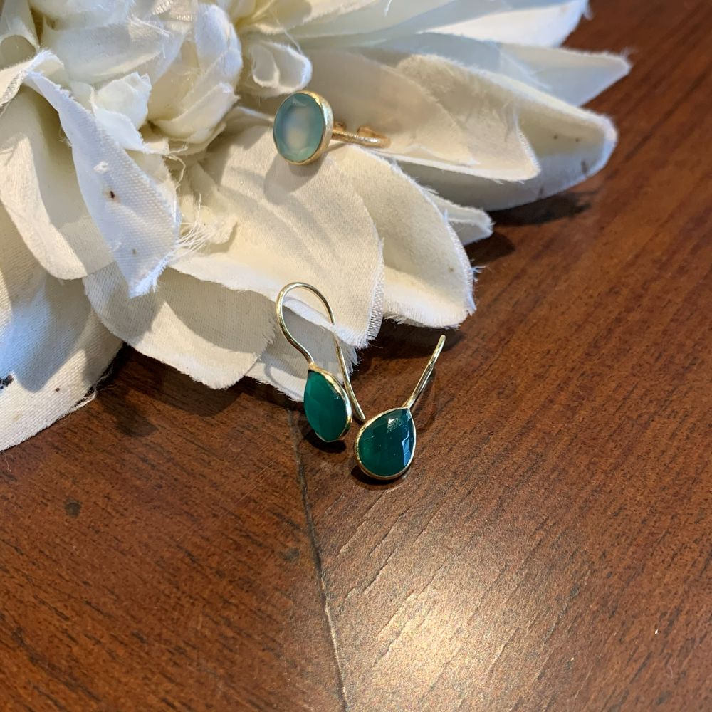Gold-tone drop earrings with oval green stones and a matching gold ring, styled on white fabric flowers over a wooden surface.