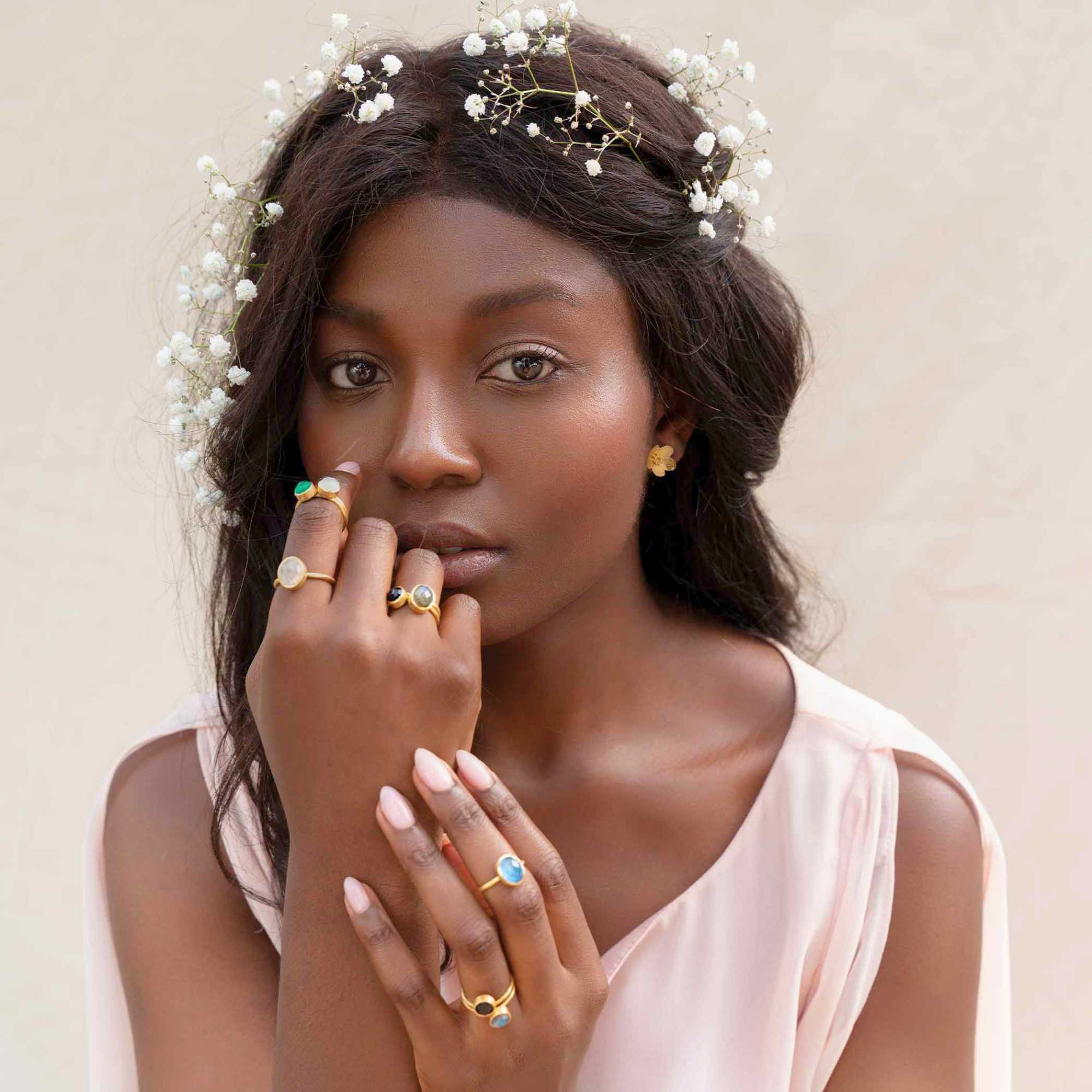 A model showcasing the Dew Drops Oval Aqua Chalcedony Adjustable Ring in gold, featuring a vibrant, bezel-set oval aqua chalcedony gemstone centered on a minimalist textured gold band, styled alongside other delicate stacking rings.