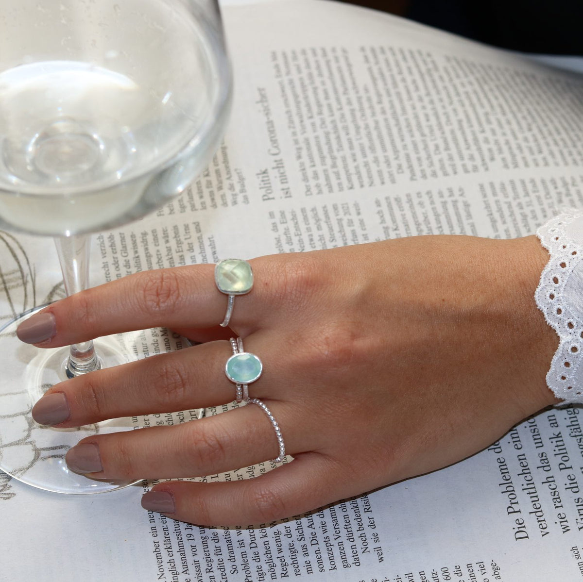Hand wearing a silver oval aqua chalcedony ring with a smooth pale blue-green gemstone and polished band, styled with delicate jewelry.