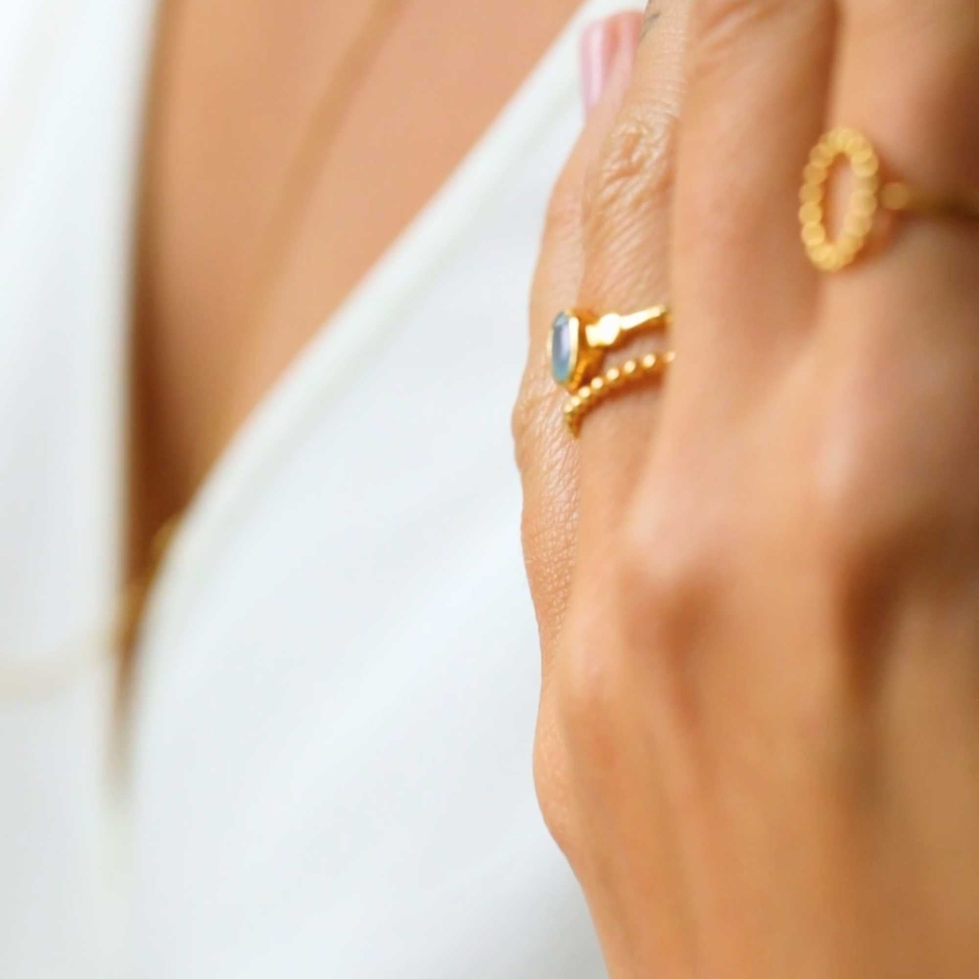 A gold adjustable ring featuring a small, bezel-set oval aqua chalcedony gemstone at its center, flanked by delicate metallic droplet accents on a smooth gold band.