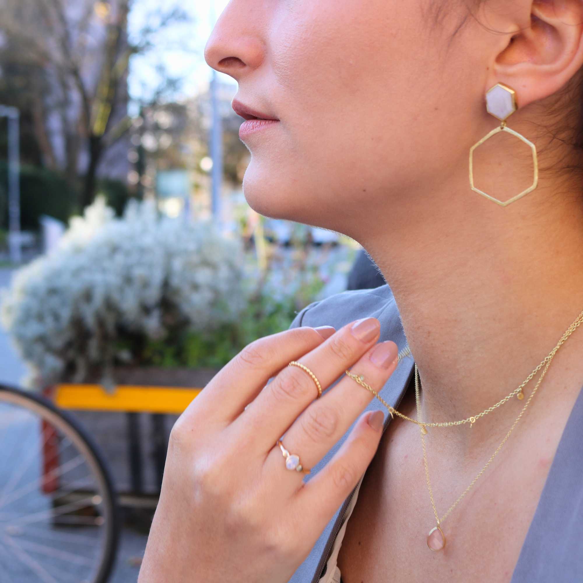 A gold adjustable ring featuring a small, bezel-set oval aqua chalcedony gemstone at its center, flanked by delicate metallic droplet accents on a smooth gold band.