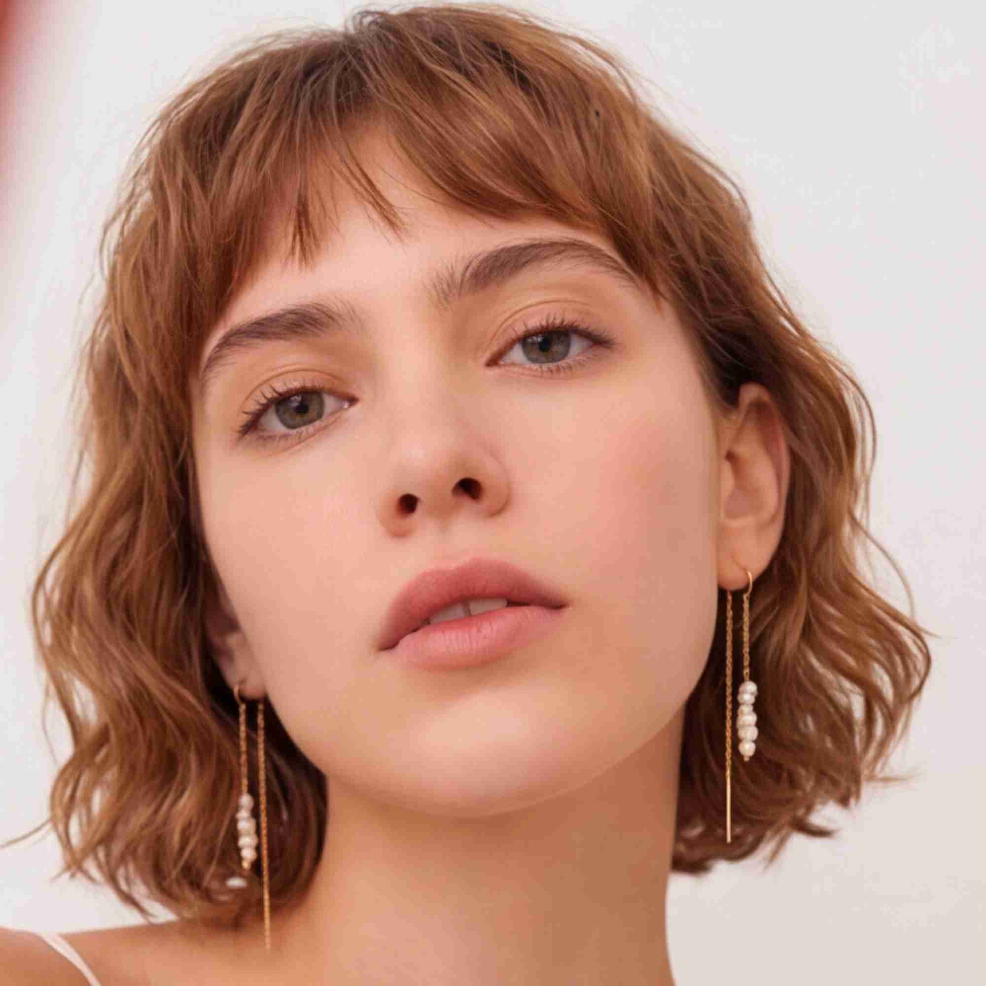 Direct eye-level portrait of a model featuring the gold stacked seed pearl chain threader earrings against a clean white background.