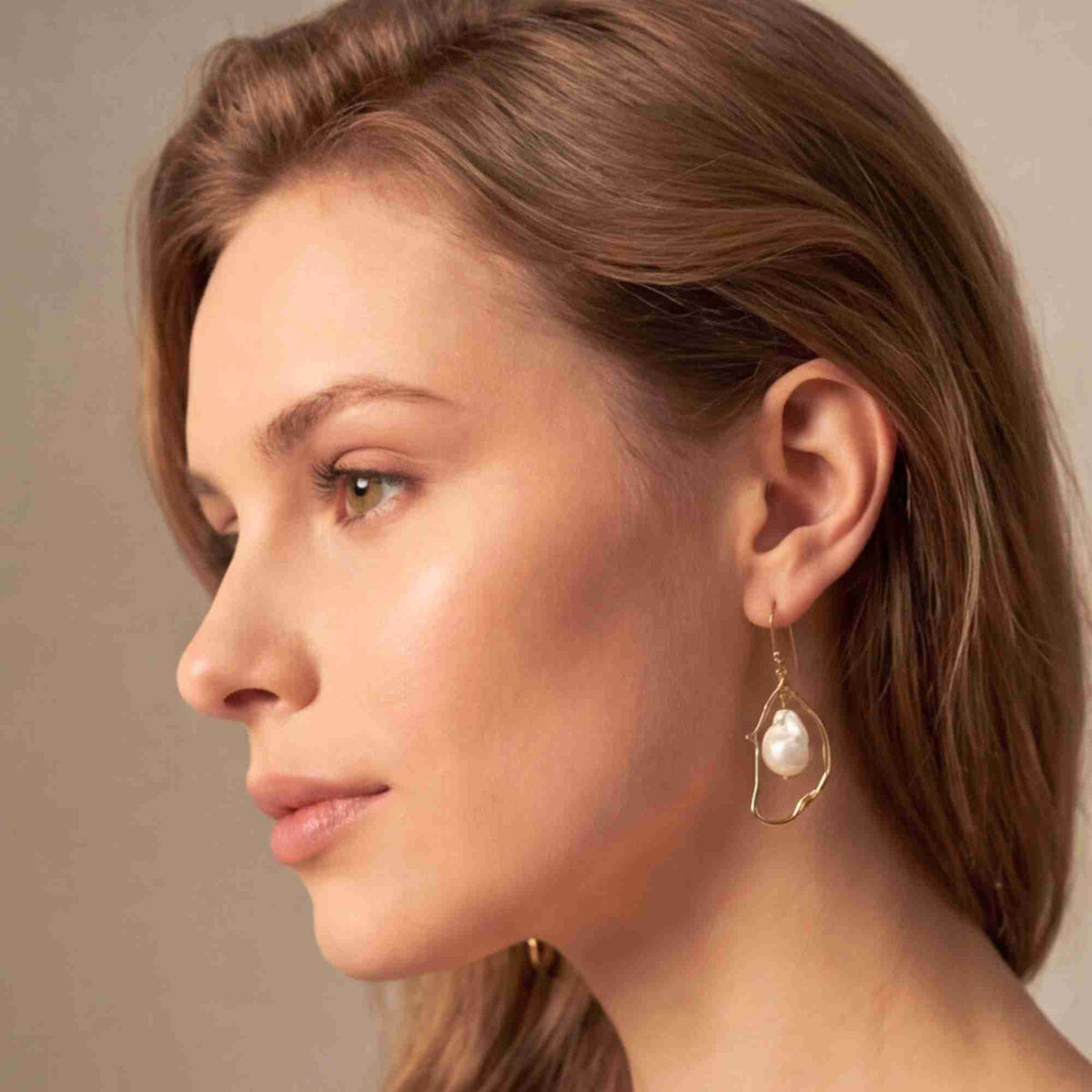 Side profile view of a light brown-haired model wearing the gold PEARLS GALORE Baroque Pearl Drop Statement Earrings, highlighting the organic gold wire frame encircling a luminous baroque pearl.