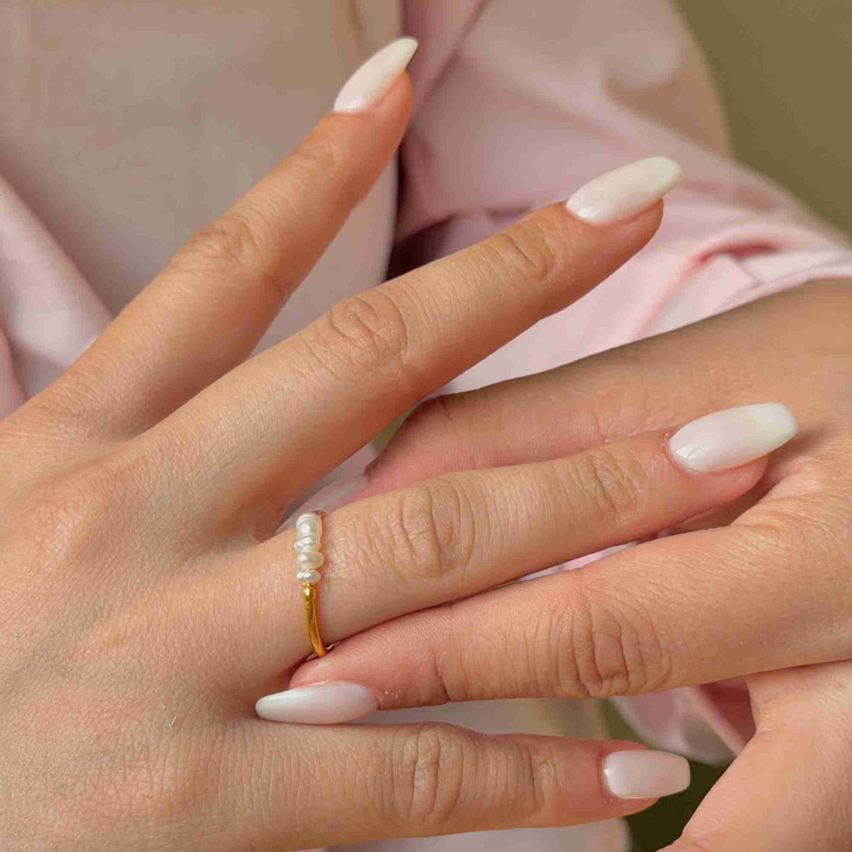 Close-up macro view of a model's hand with manicured white nails showing the delicate gold band set with a horizontal row of small seed pearls.