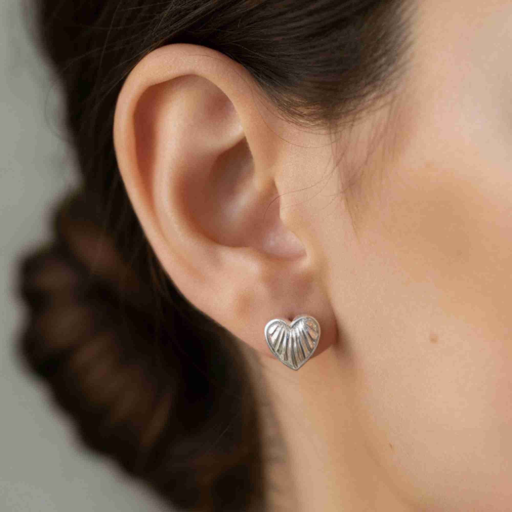 Macro close-up shot of a model's ear showing the silver Queen of Charms Fluted Heart Stud Earring, highlighting the ribbed texture and high-shine polished finish.