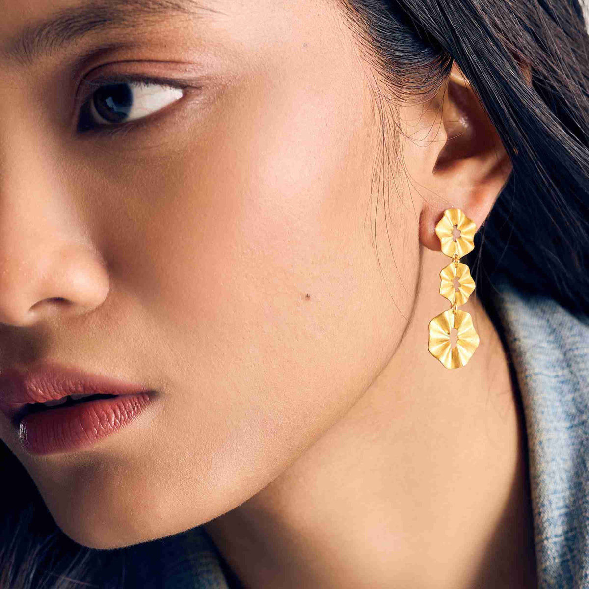 Close-up three-quarter portrait of a dark-haired model wearing three tiered gold pleated discs