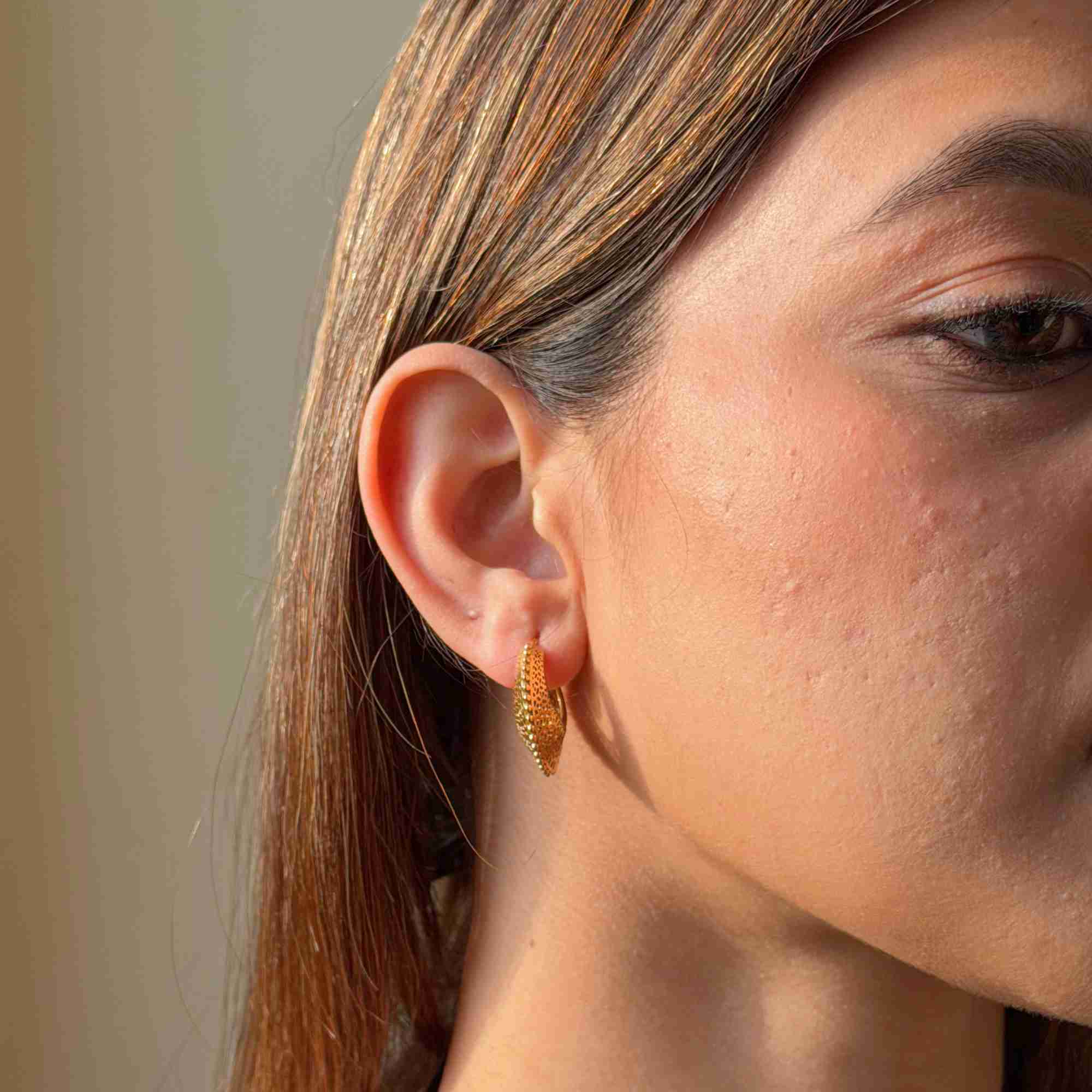 Front-angled close-up of a model wearing the gold Ribbons & Lace Filigree Sculptural Hoop Earrings, showcasing the tapered, textured front profile under warm natural lighting.