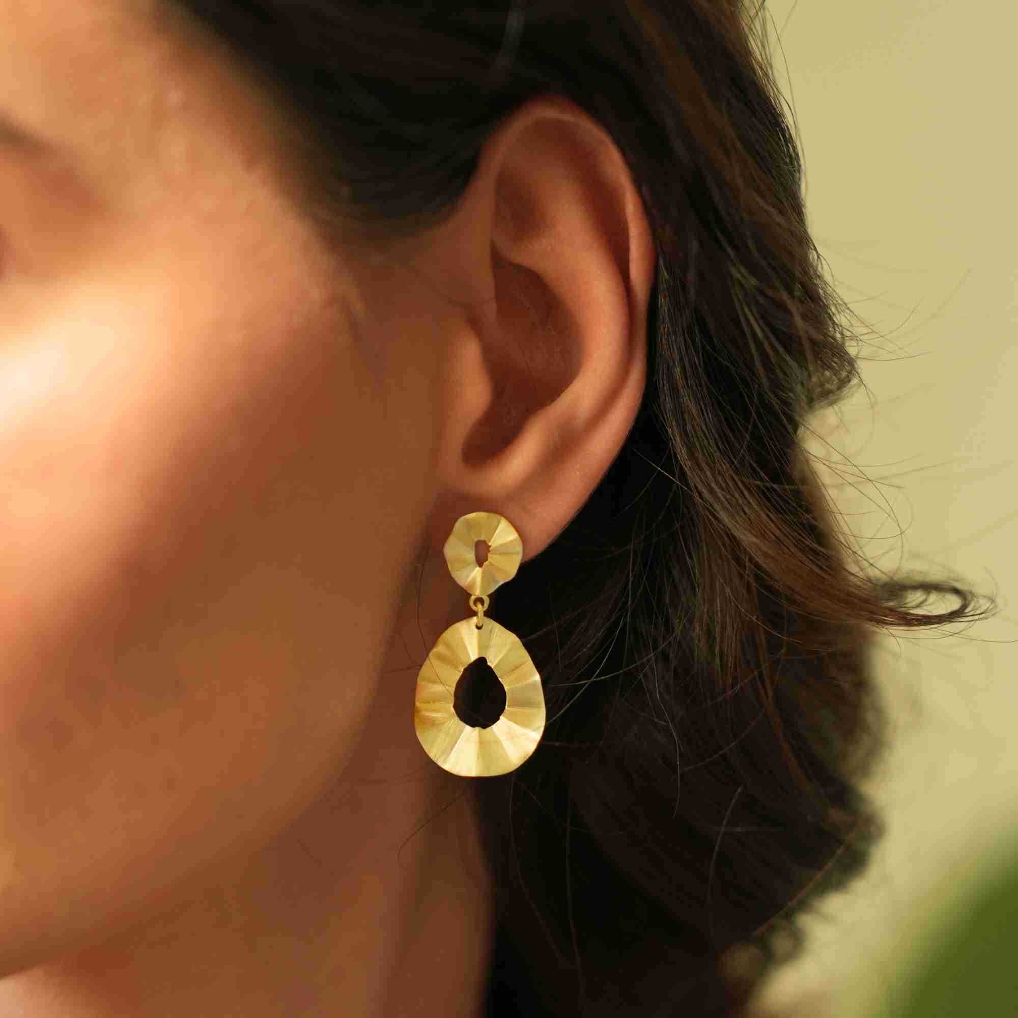 Side profile view of a brunette model wearing the gold-plated Ribbons & Lace Ruffle Fold Drop Statement Earrings in warm, natural lighting.
