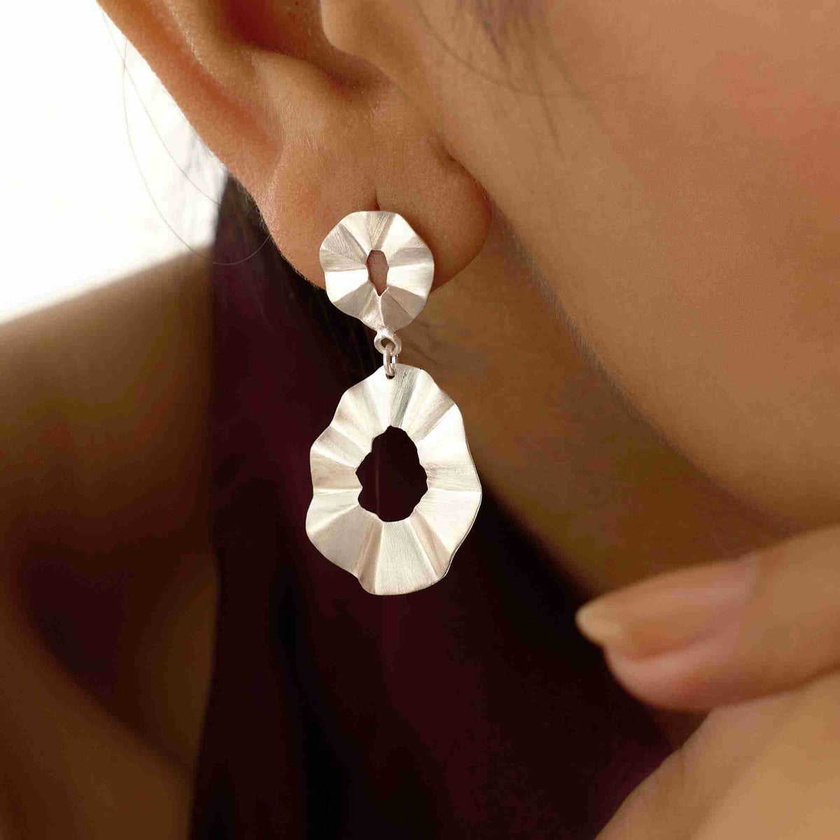 Macro close-up shot focused on the ear showing the intricate ruffled, folded texture of the silver double-drop statement earrings against a dark top.