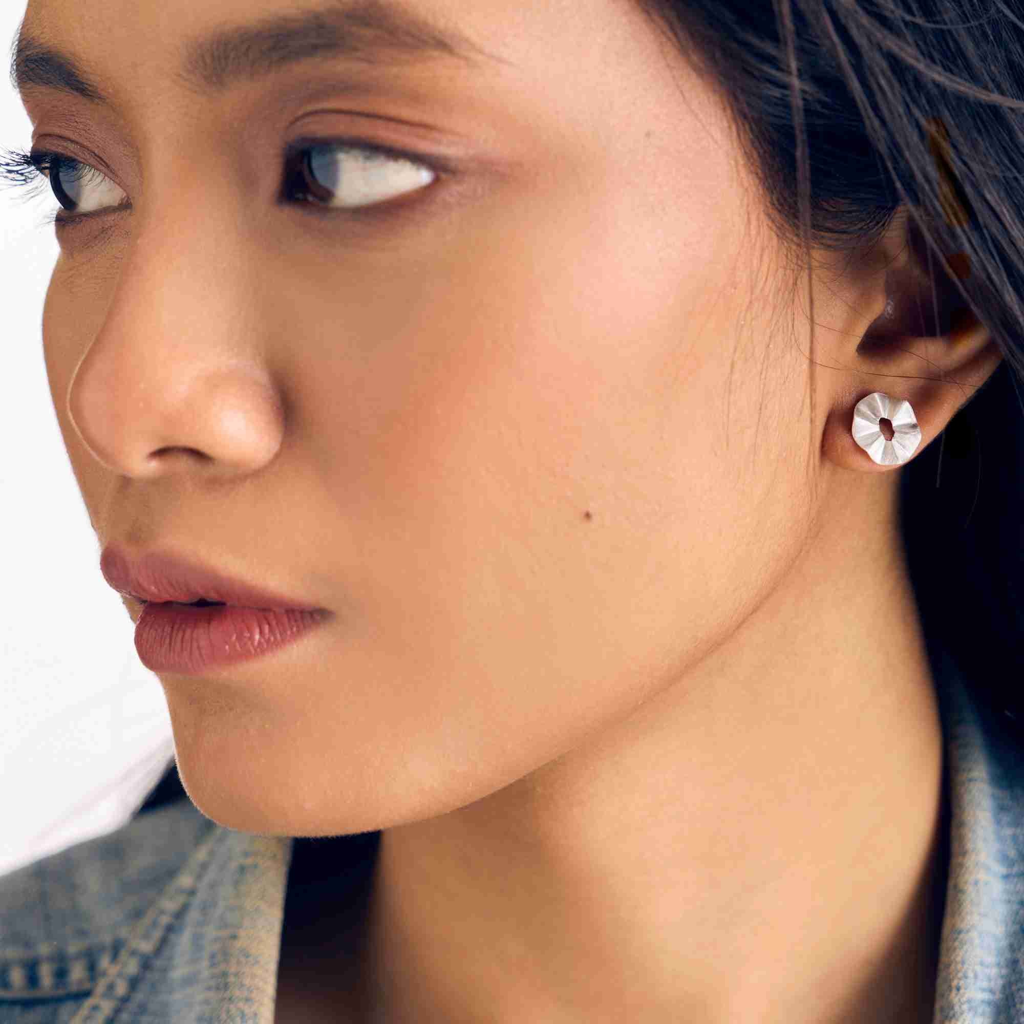 Close-up model view named Ribbon & Lace (2).jpg showing a woman wearing the Ribbons & Lace Ruffle Fold Stud Earrings Silver, showcasing the textured, hand-brushed matte silver finish shaped into a delicate, three-dimensional ruffled fold design by Protsaah Zurich.