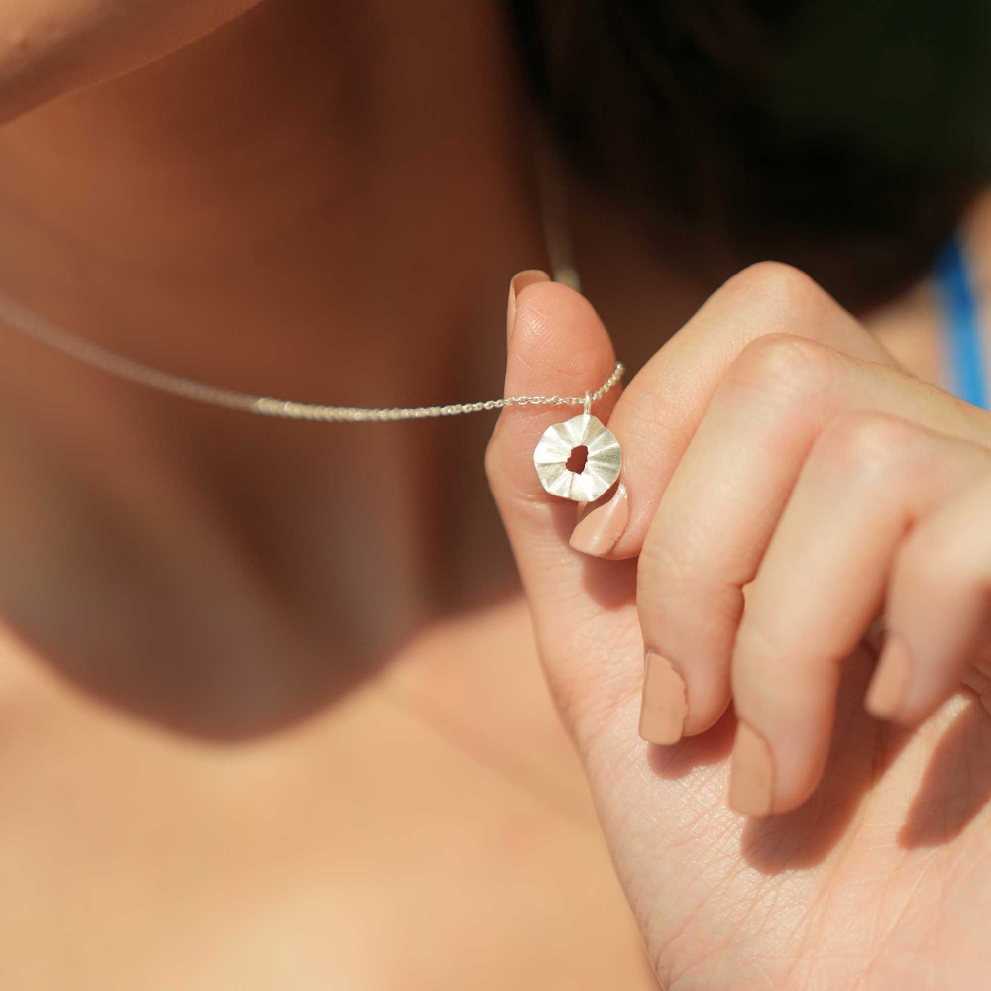 A model wearing the Ribbons & Lace Ruffle Furls Pendant Necklace in silver, showcasing a delicately textured, organic ruffled disc pendant suspended from a fine silver chain.