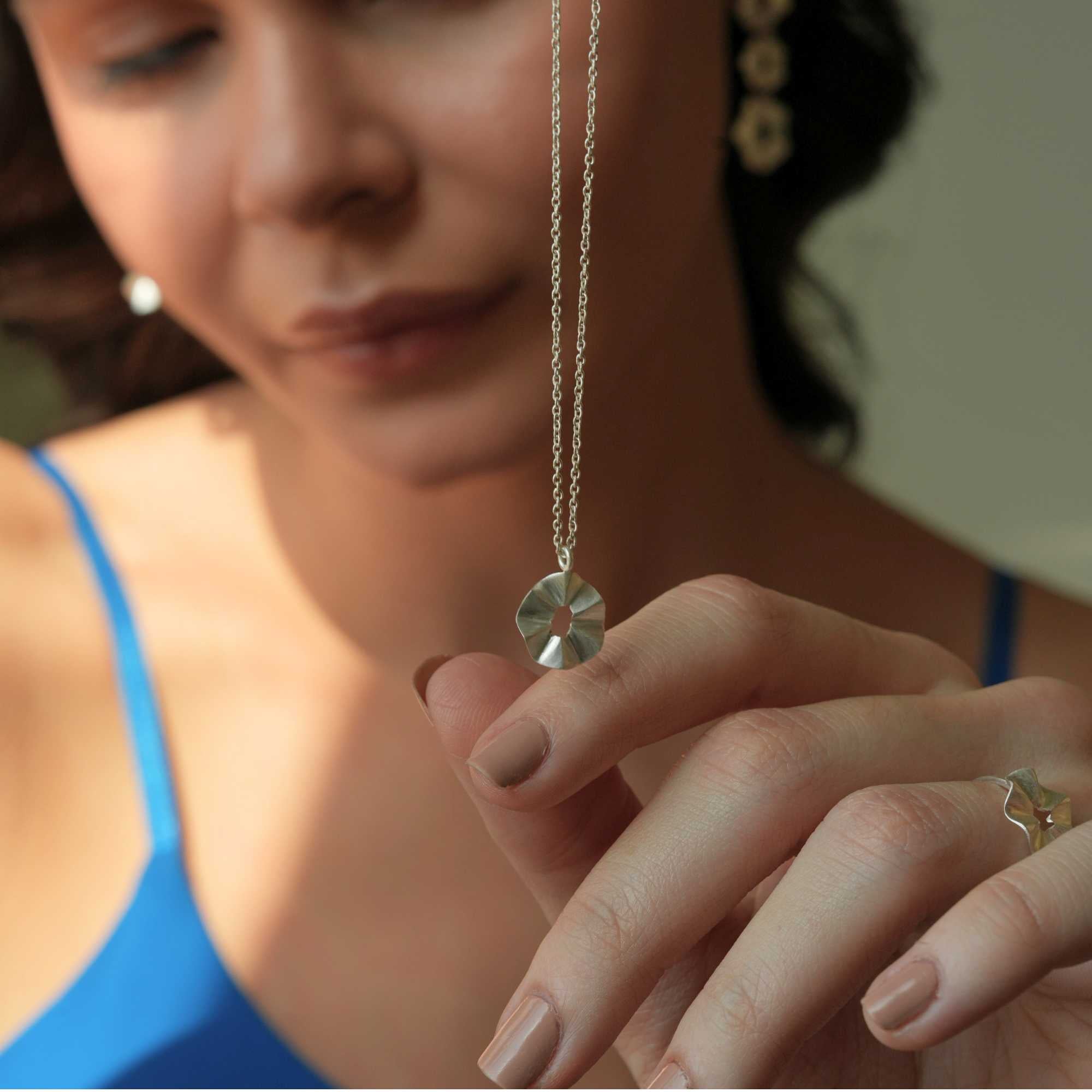 A model wearing the Ribbons & Lace Ruffle Furls Pendant Necklace in silver, showcasing a delicately textured, organic ruffled disc pendant suspended from a fine silver chain.