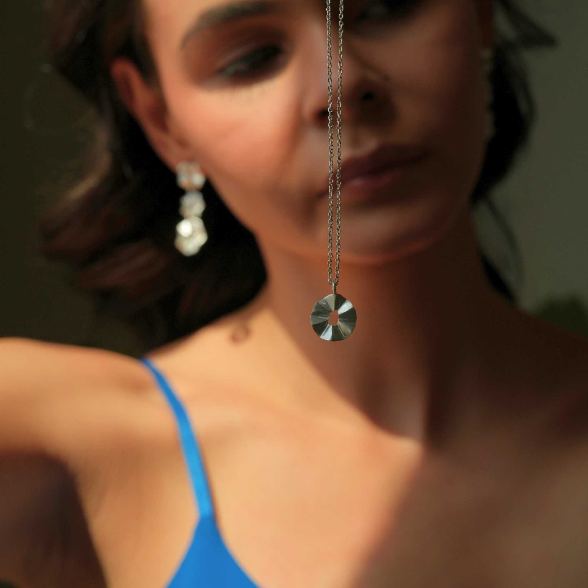 A model wearing the Ribbons & Lace Ruffle Furls Pendant Necklace in silver, showcasing a delicately textured, organic ruffled disc pendant suspended from a fine silver chain.