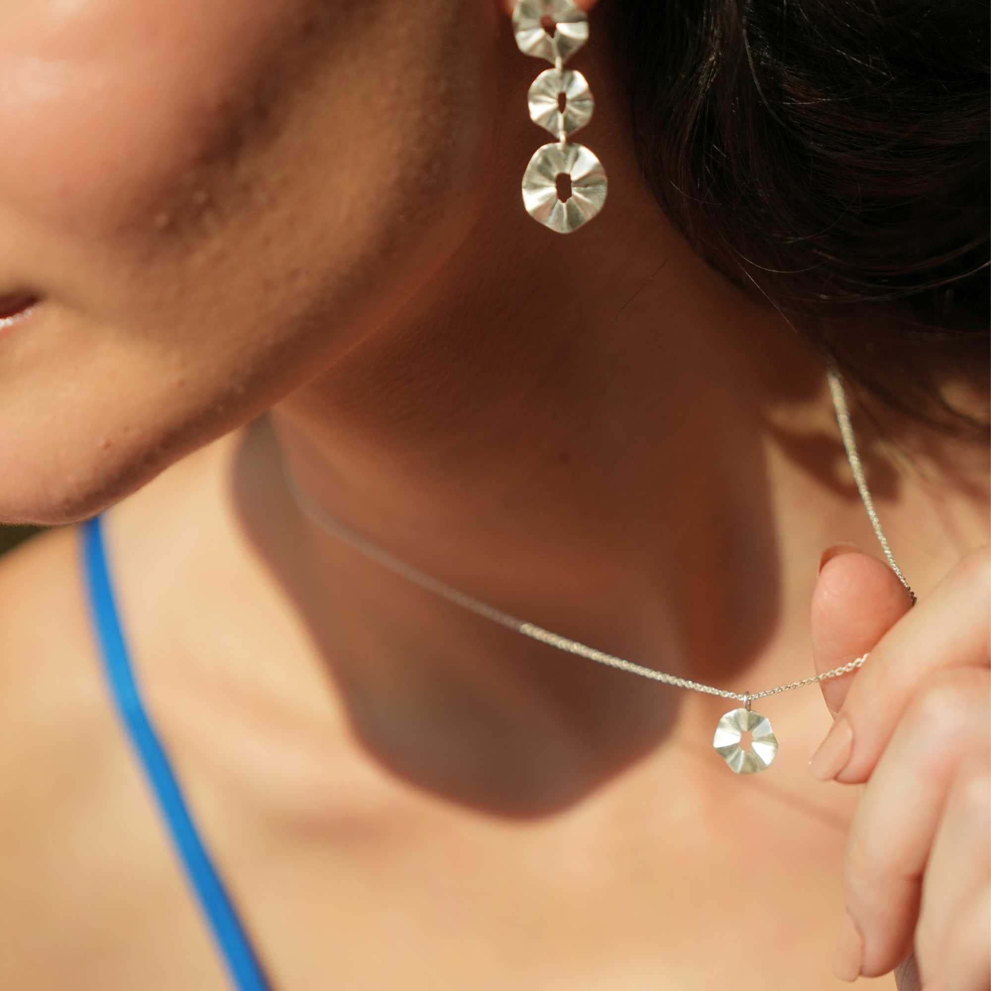 A model wearing the Ribbons & Lace Ruffle Furls Pendant Necklace in silver, showcasing a delicately textured, organic ruffled disc pendant suspended from a fine silver chain.