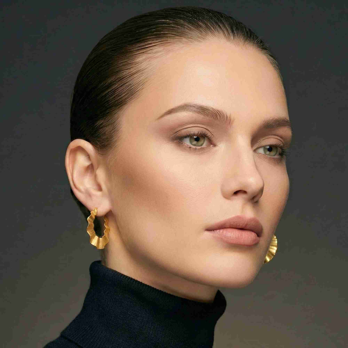 Portrait studio d'un mannequin au chignon lisse et col roulé sombre, larges créoles dorées ondulées