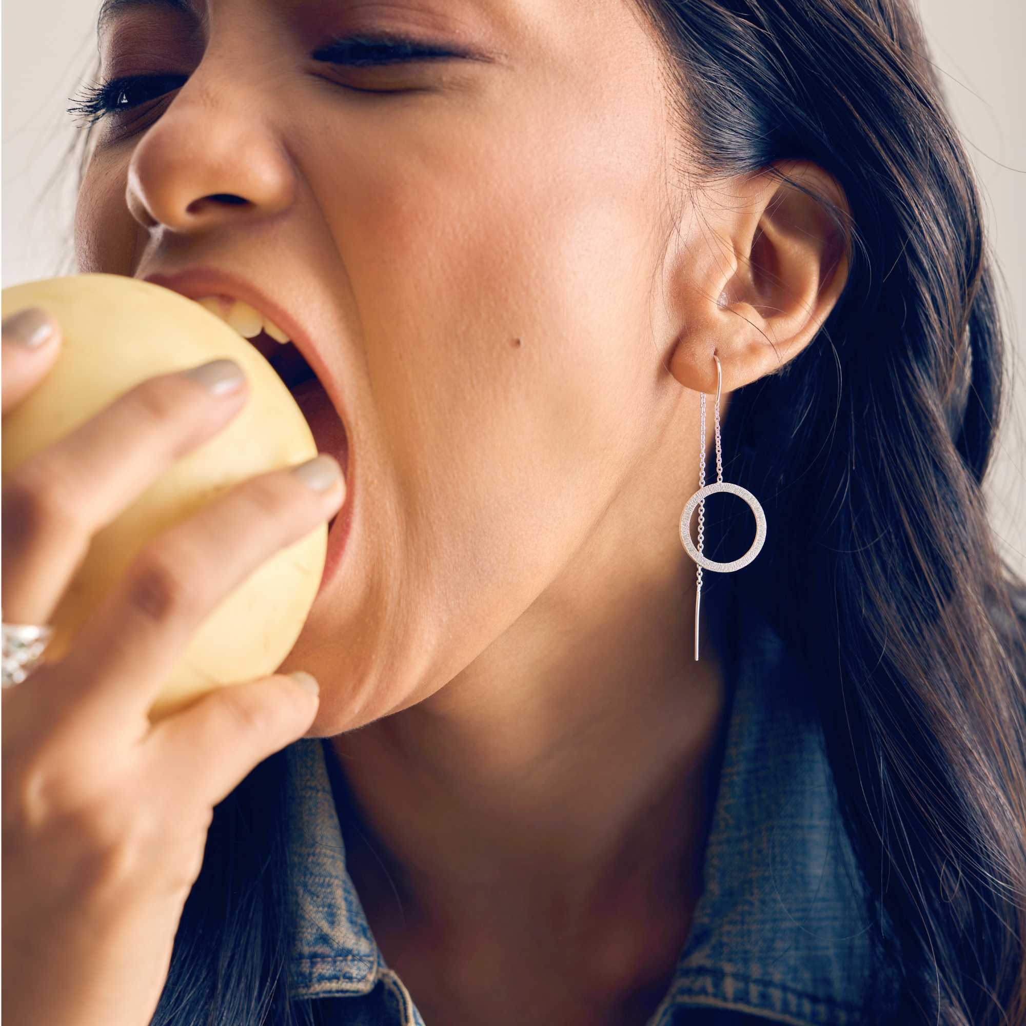 A model showcasing the Shimmering Disks Circle Chain Threader Earrings in silver, featuring a delicate fine drop chain that threads through the earlobe to suspend a textured, brushed metallic circular geometric charm.
