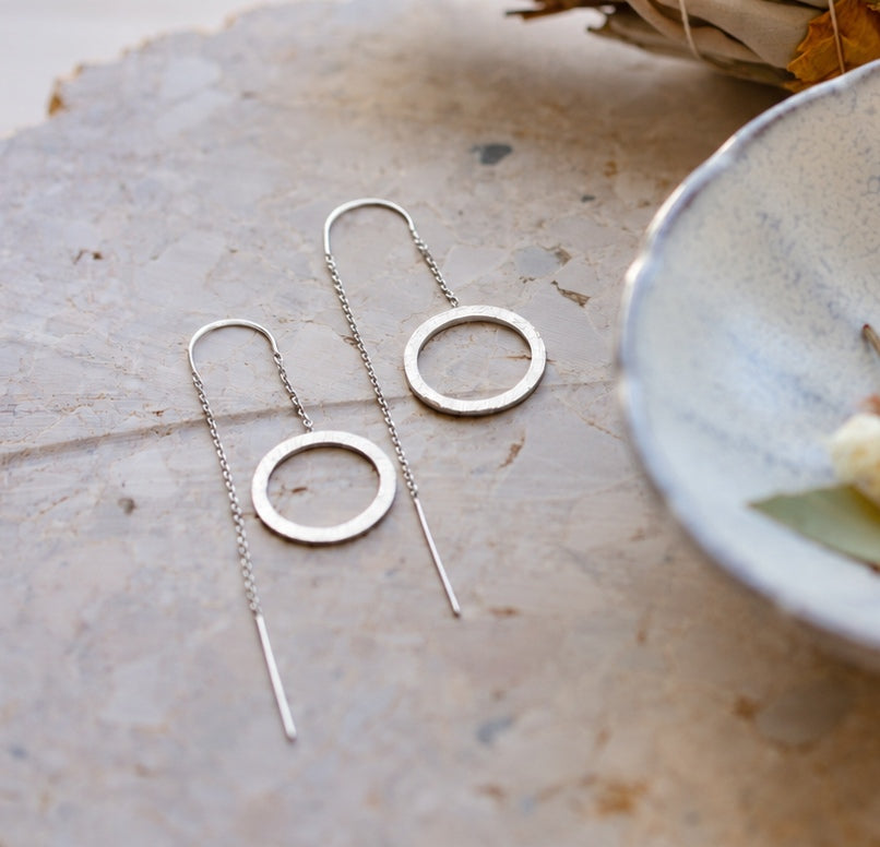 Circle chain threader earrings in Silver with a hand-brushed finish lying on a pale stone surface