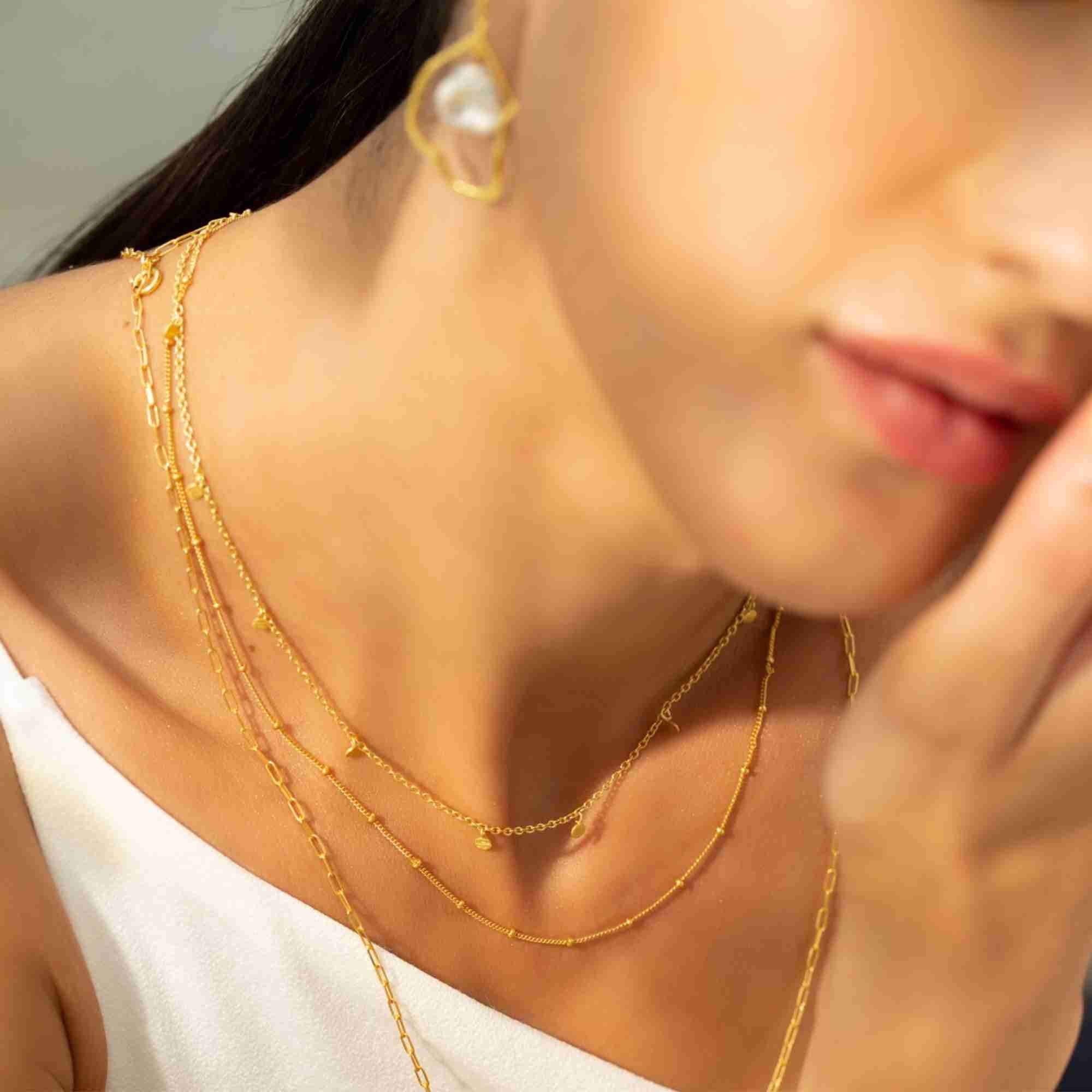 Close-up shot showing the gold Shimmering Disks Constellation Disc Chain Necklace layered with other delicate gold chain styles against a white top.