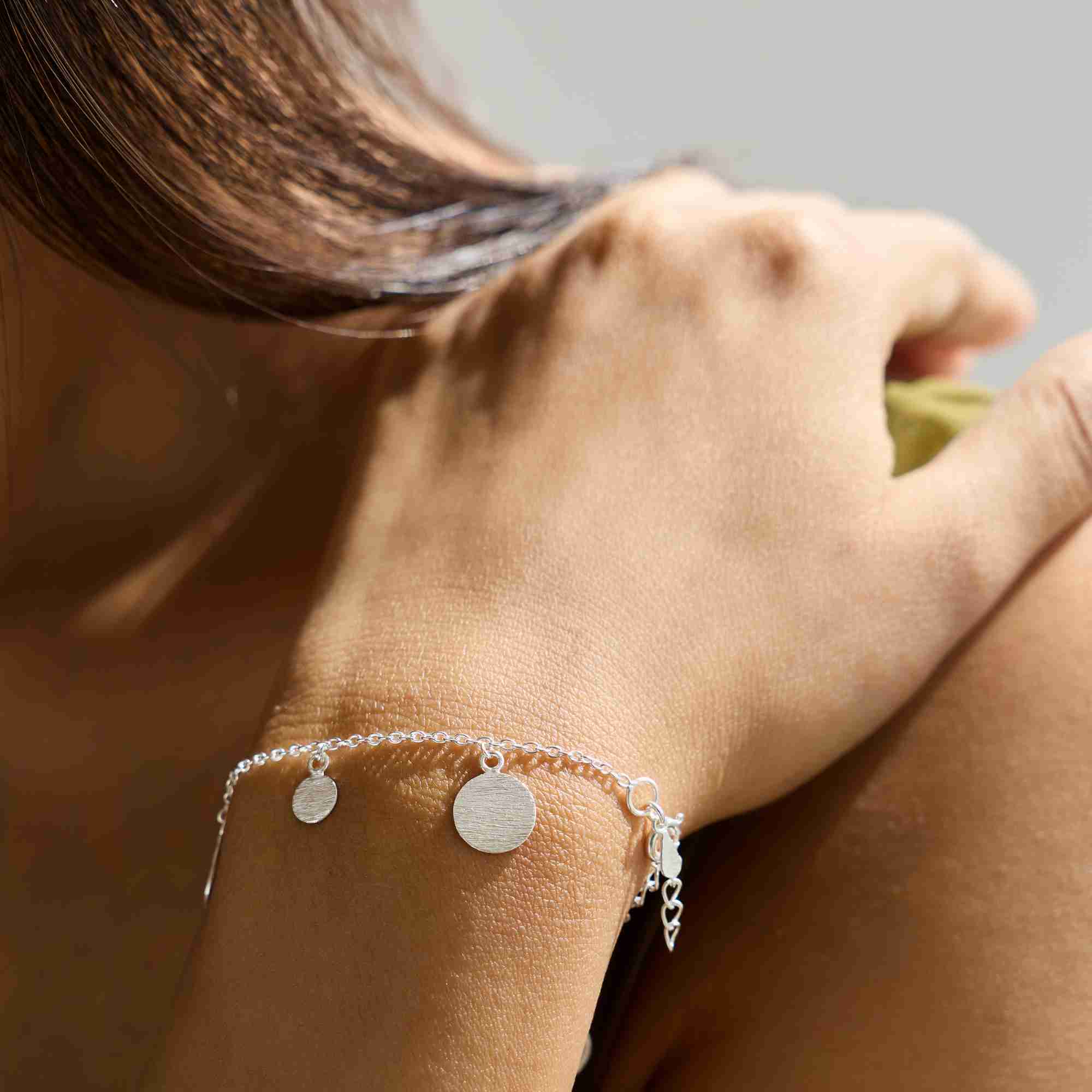 Macro view of the silver Shimmering Disks Delicate Chain Bracelet on a wrist, highlighting the textured finish of the circular disc drops and adjustable clasp.