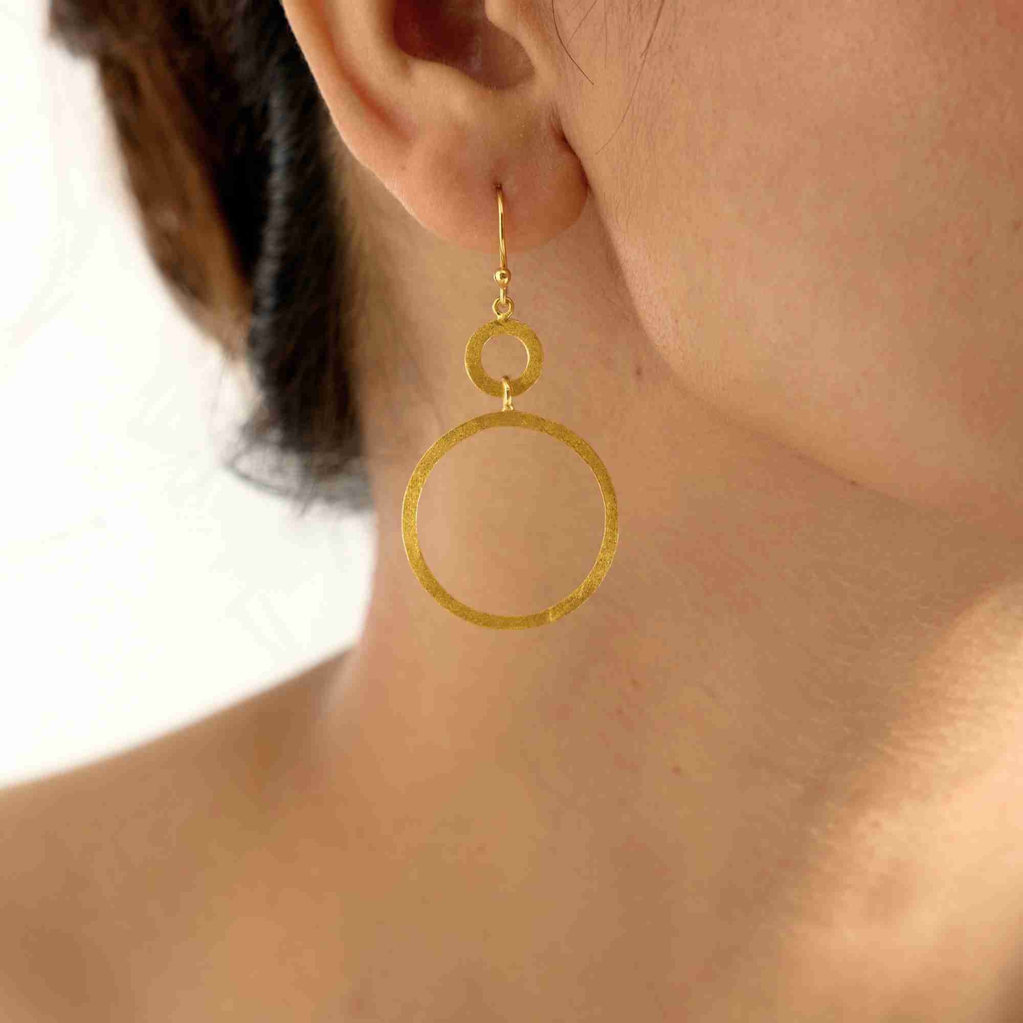 Detailed arrangement view of a pair of Shimmering Disks Dual Circle Statement Earrings Gold resting on a clean white surface, showcasing their bold sculptural silhouette and rich gold luster.