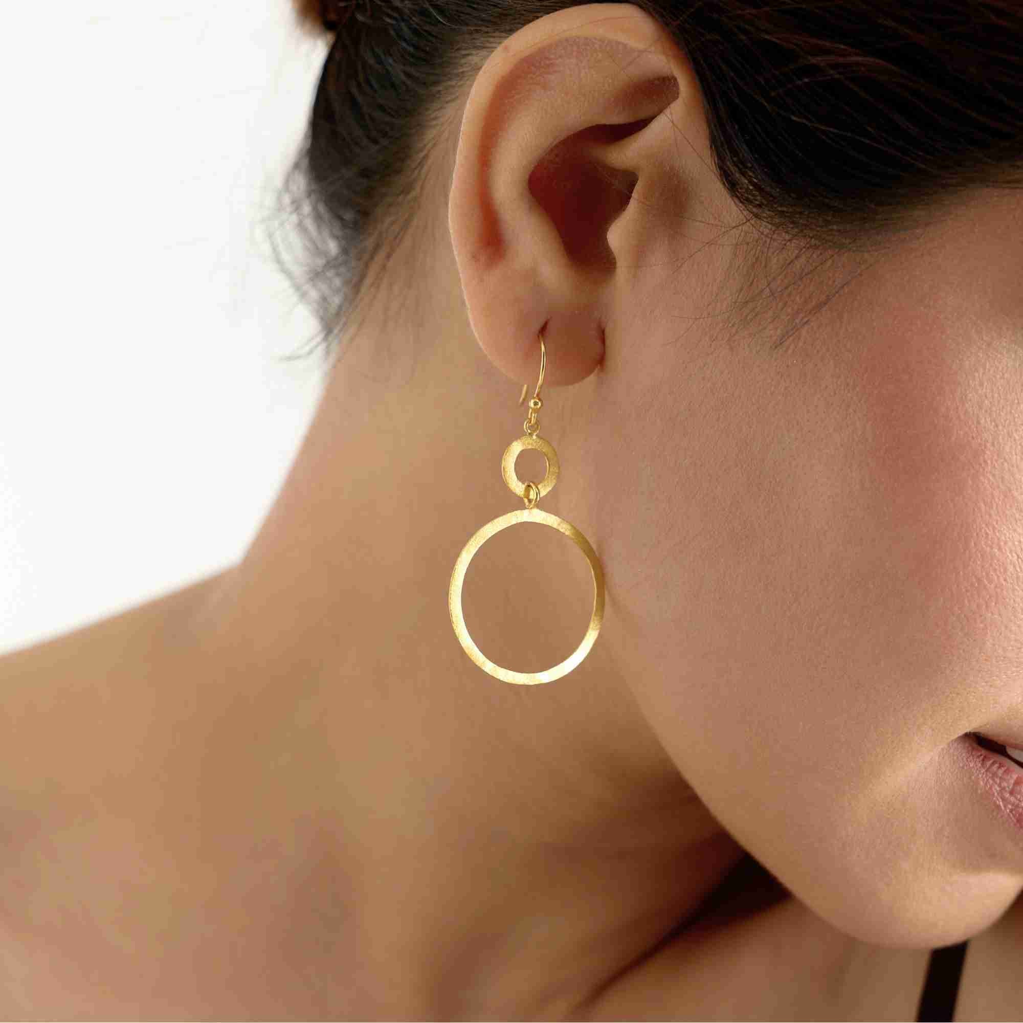 Close-up product view of Shimmering Disks Dual Circle Statement Earrings Gold, highlighting the intersecting geometric double-circle design and artisanal hand-applied scratch texture.