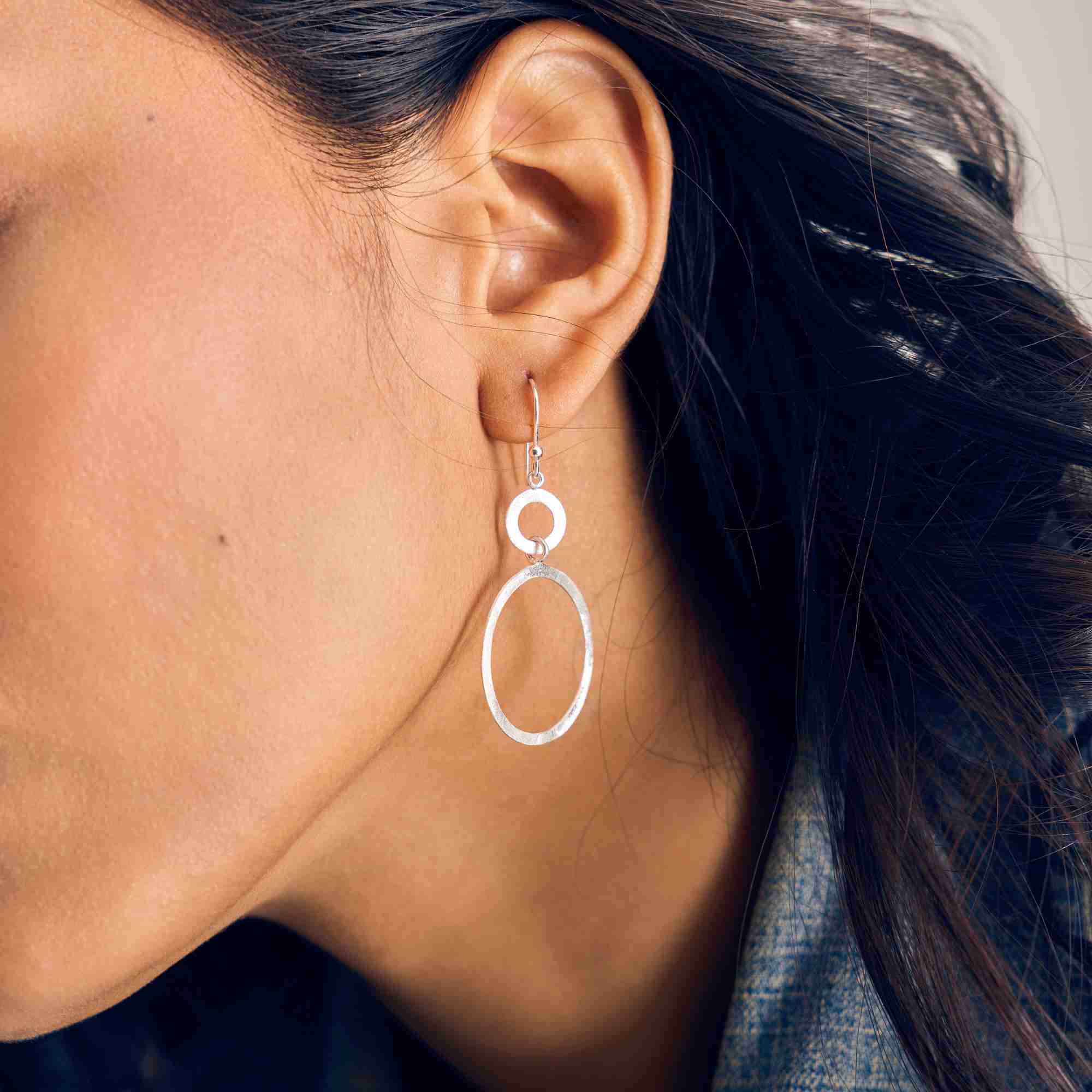 Model wearing Shimmering Disks Dual Circle Statement Earrings Silver, showcasing how the interconnected, overlapping double circular discs drape elegantly on the earlobe with a soft matte silver luster.