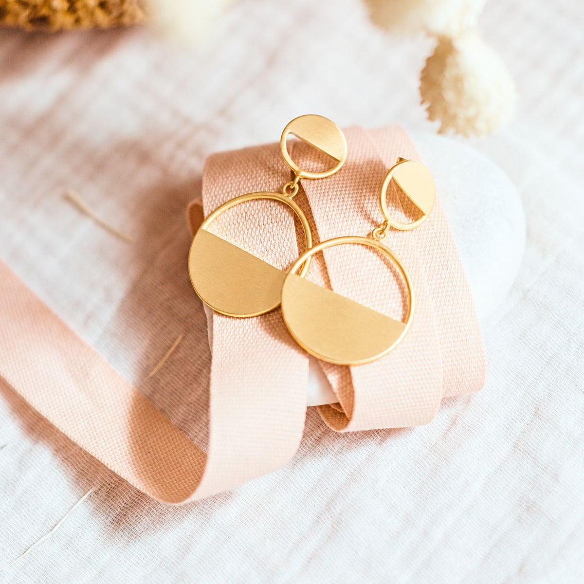 Horizon Half-Moon Drop earrings in gold with a smooth matte finish draped over a blush ribbon