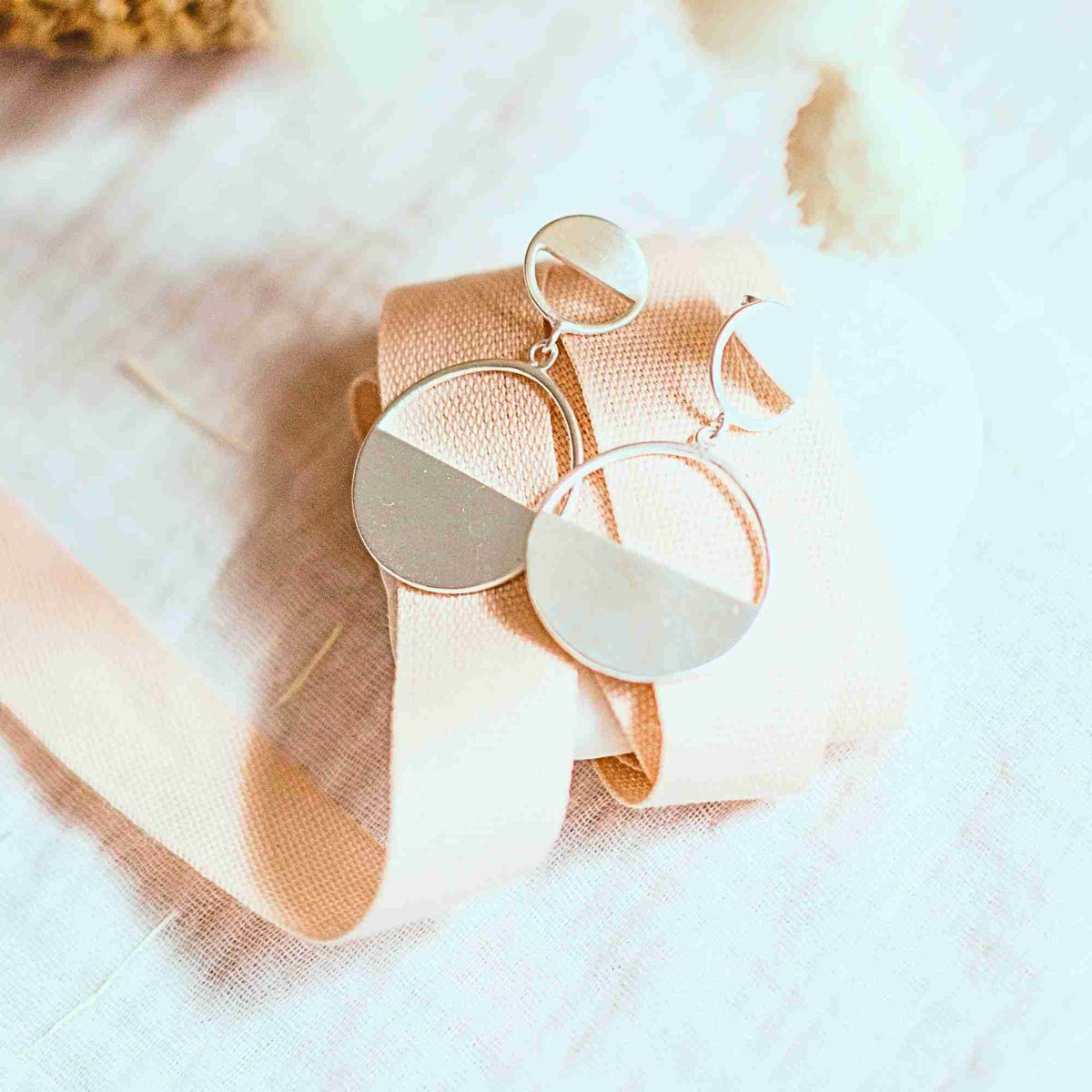 Horizon Half-Moon Drop earrings in silver with a smooth matte finish draped over a blush ribbon