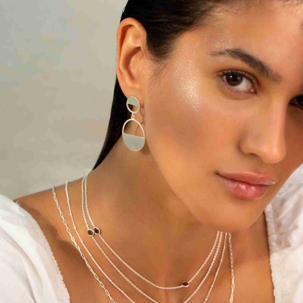 Model with sleek dark hair wearing a Horizon Half-Moon Drop earring in silver, with layered silver chains