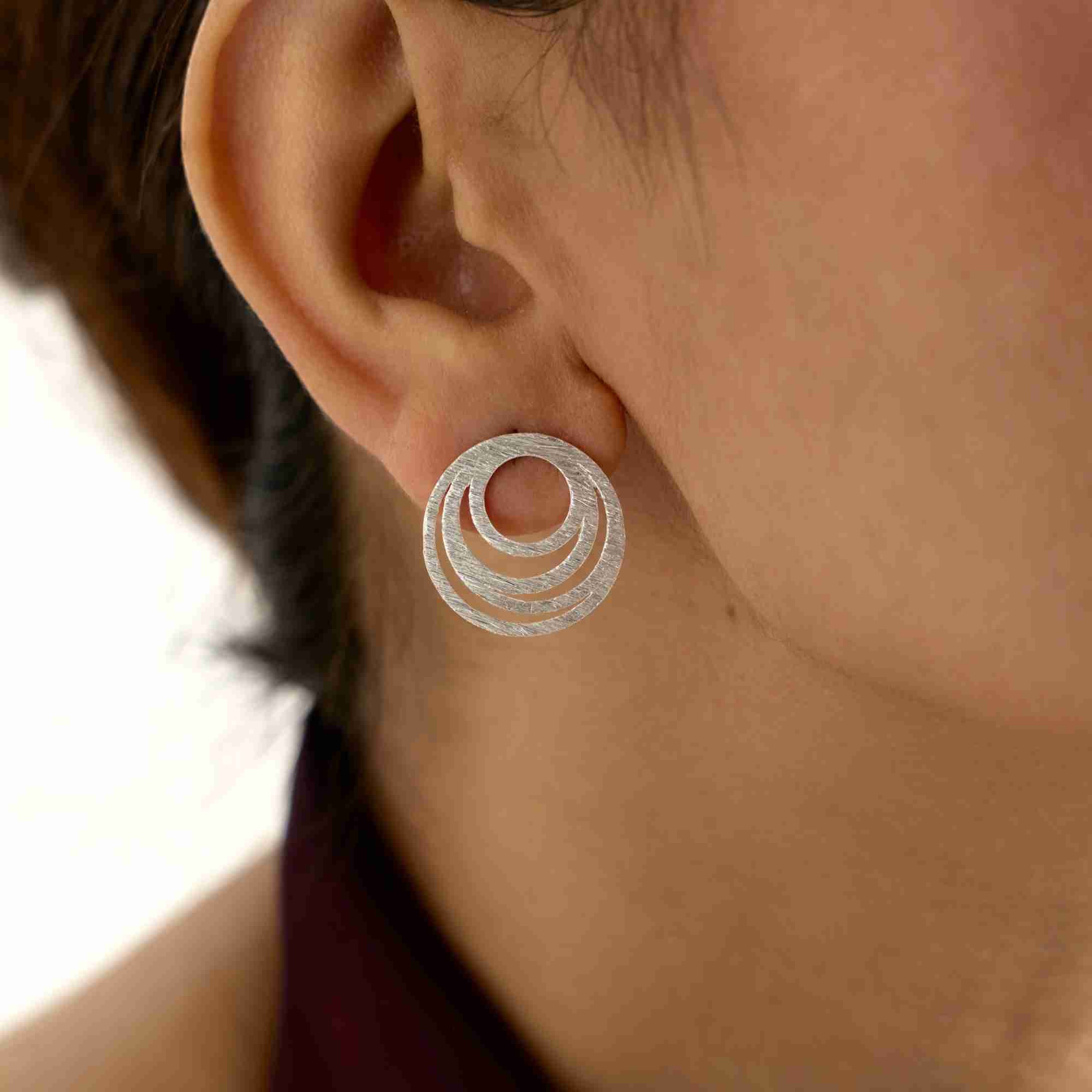 Extreme close-up of the silver Shimmering Disks Intermingled Circles Stud Earring, highlighting the hand-brushed textured surface and openwork design.