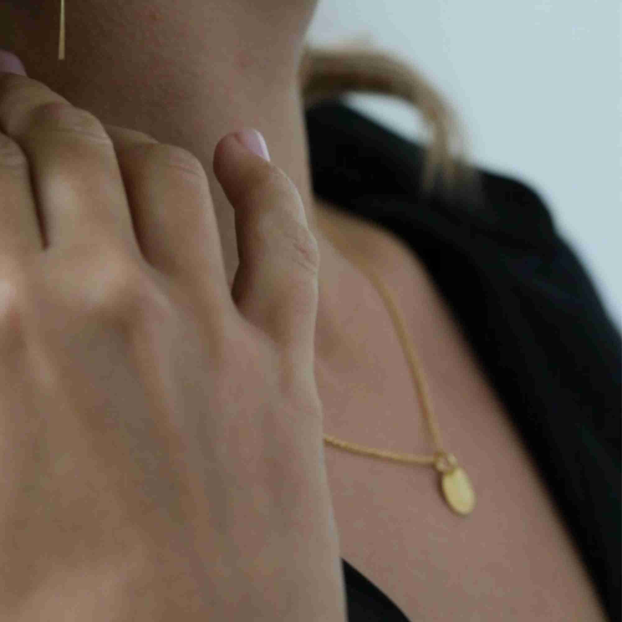 Model with hand resting near neck, showing the gold Shimmering Disks Minimalist Coin Pendant Necklace resting softly along the collarbone.