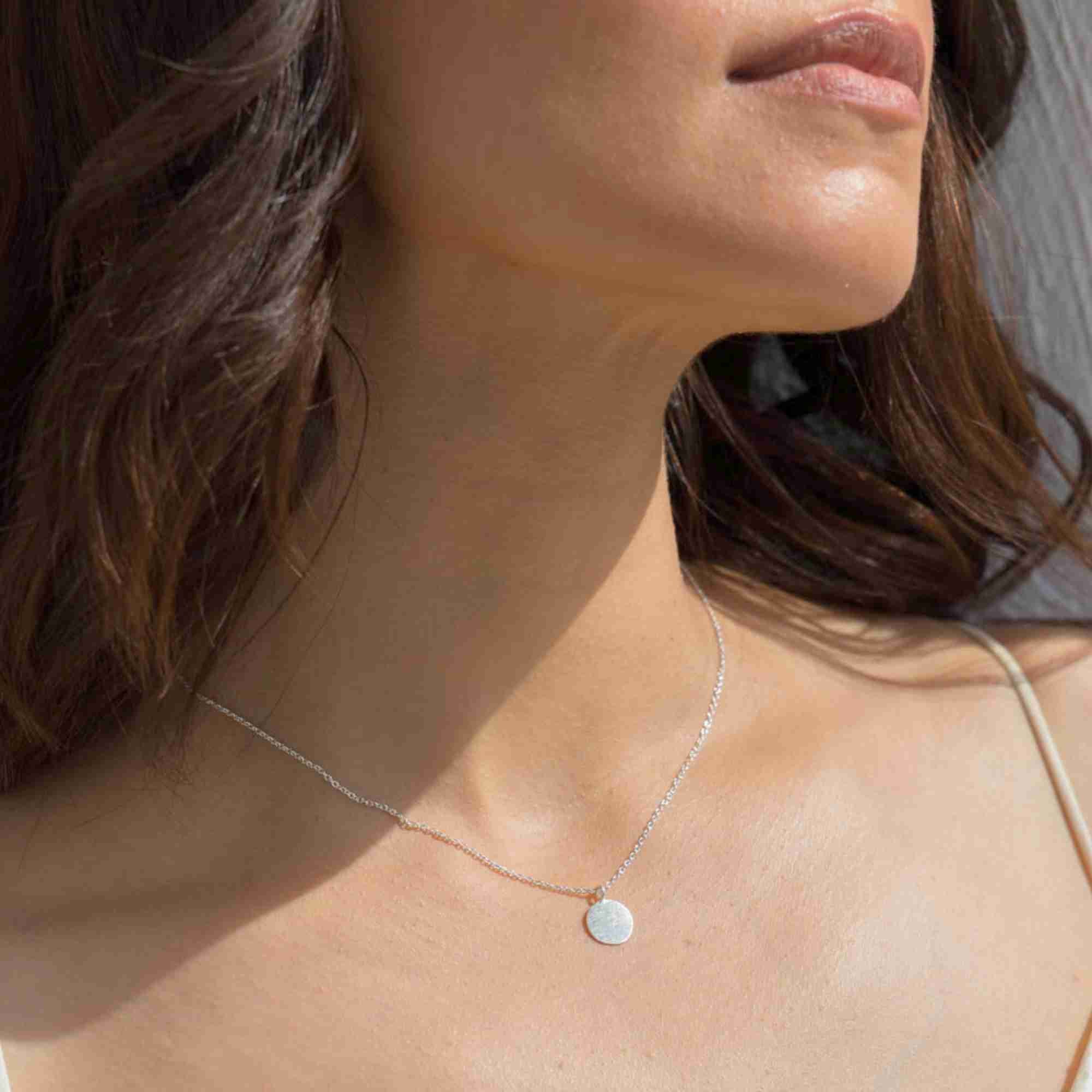 Side-angled shot of a model wearing the silver Shimmering Disks Minimalist Coin Pendant Necklace resting gracefully along her collarbone.