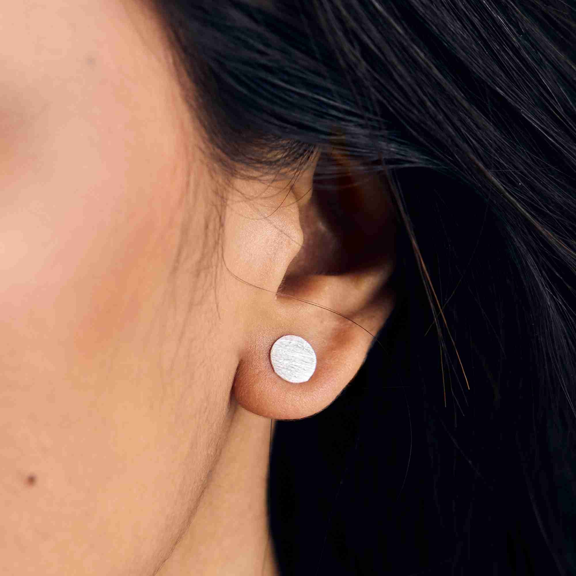 Detailed macro shot of the sterling silver Shimmering Disks Minimalist Stud Earring on a model's ear, showing the hand-applied textured surface.