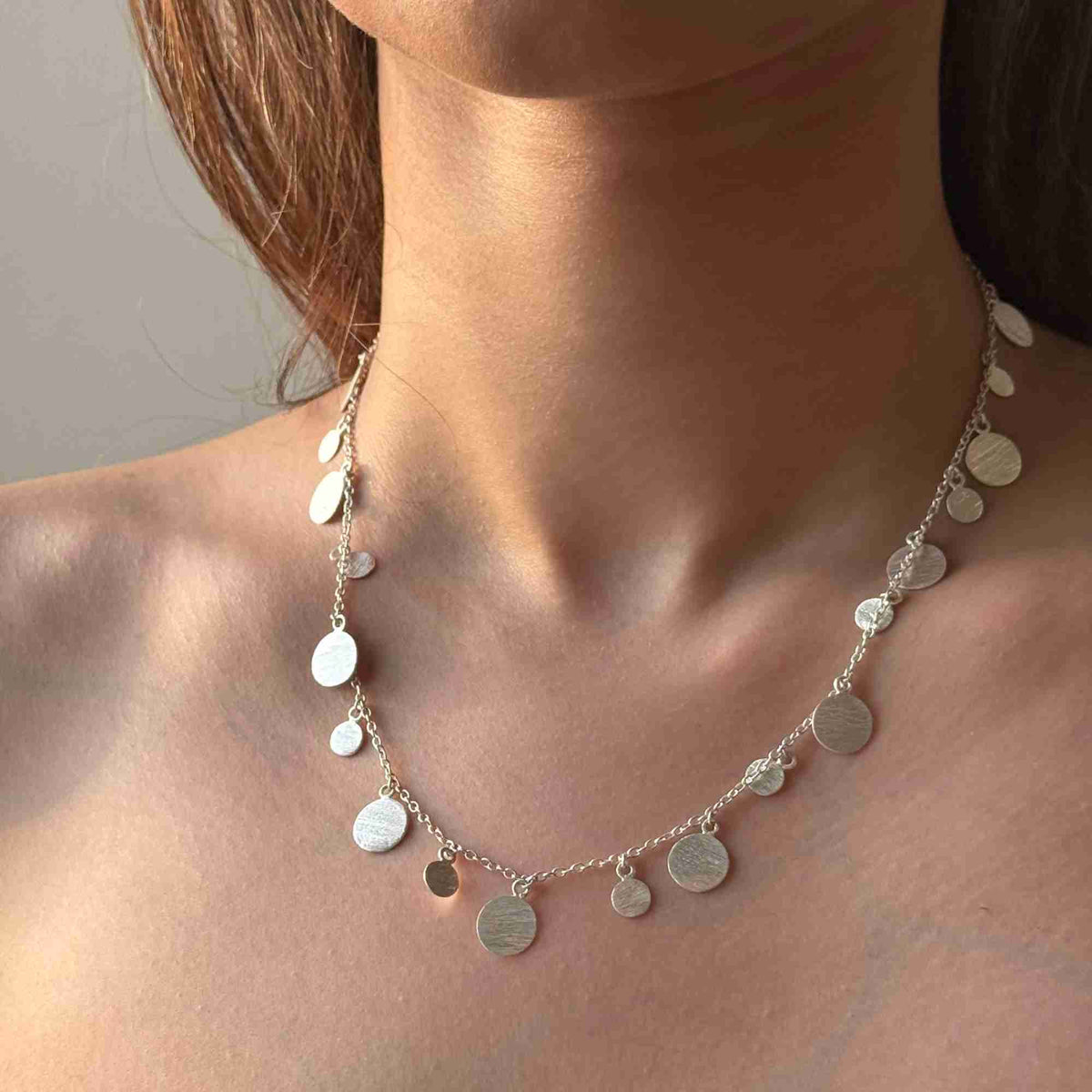 Model wearing scattered disc necklace in silver along the collarbone, bare shoulders