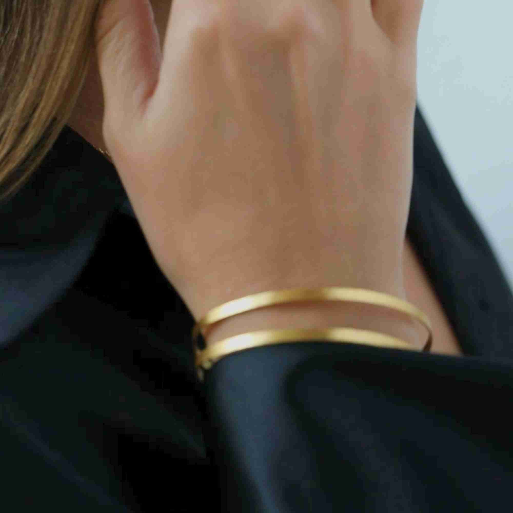 Model resting her hand near her collar while wearing the gold Shimmering Disks Sculptural Flat-Band Double Cuff over a black silk blouse.