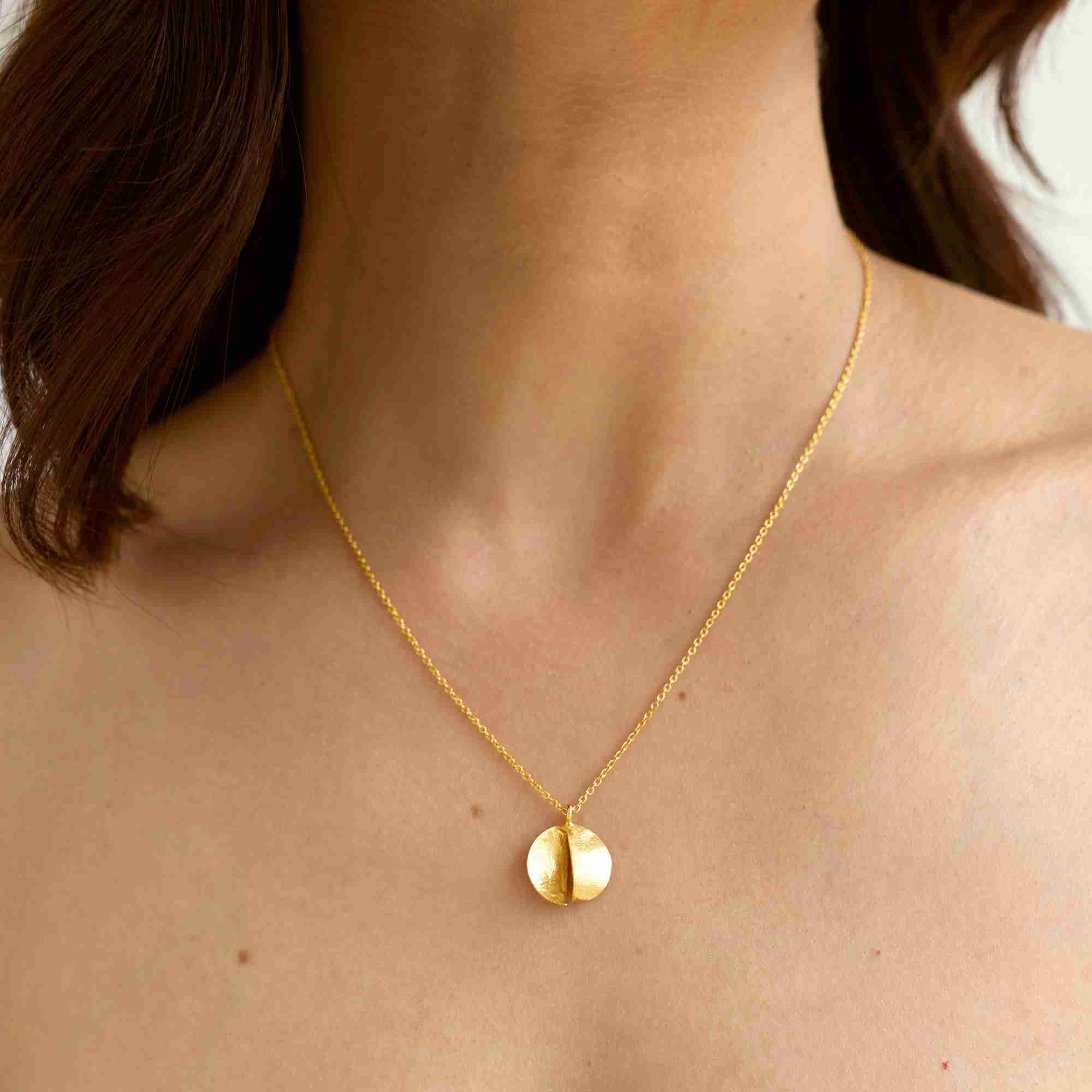 Close-up shot highlighting the gold Shimmering Disks Split-Disc Pendant Necklace resting on a collarbone, detailing its dimensional folded disc pendant and brushed gold texture.
