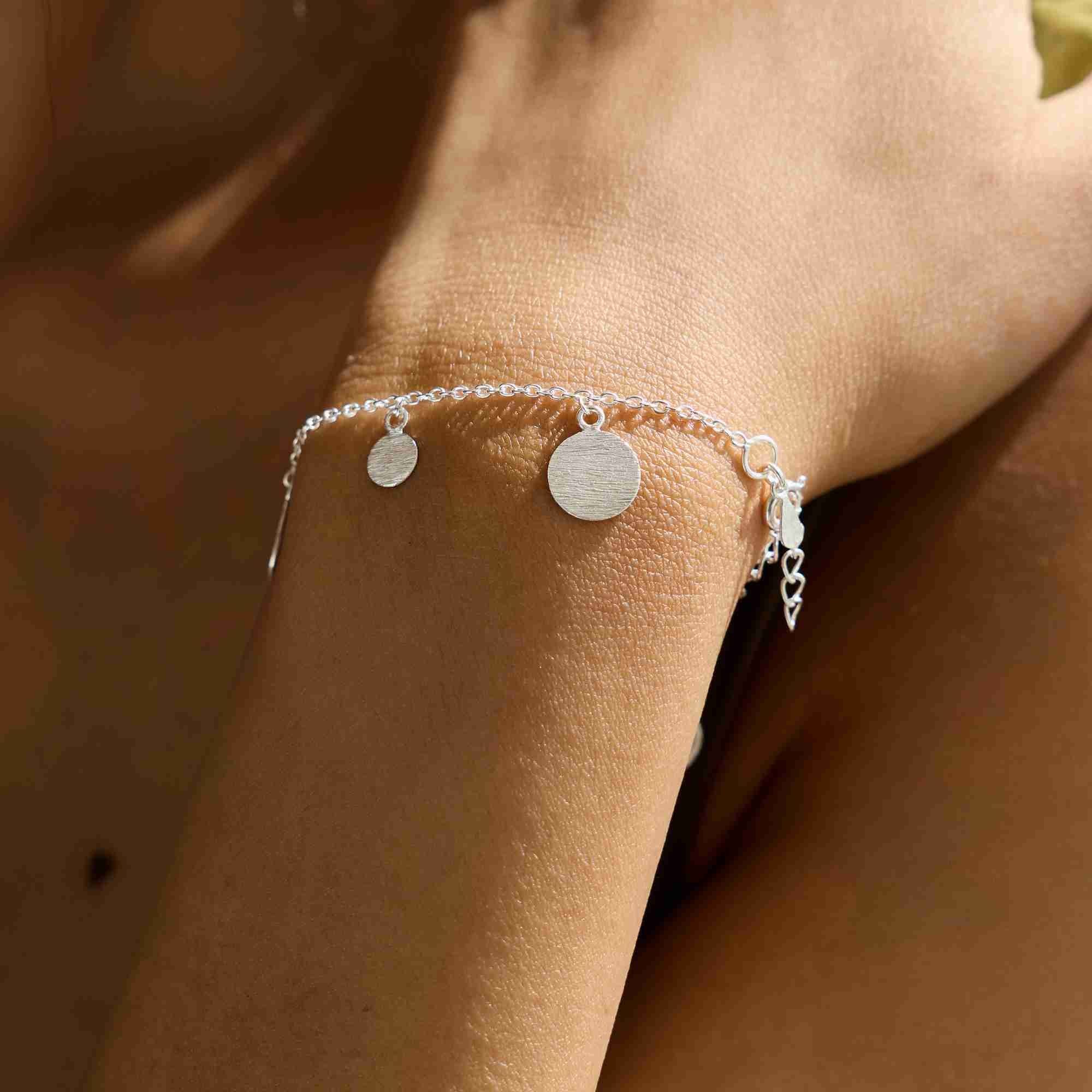 Model wearing the Shimmering Disks Delicate Chain Bracelet Silver, showing the minimalist fine trace chain and the central textured silver disc element resting elegantly on the wrist.