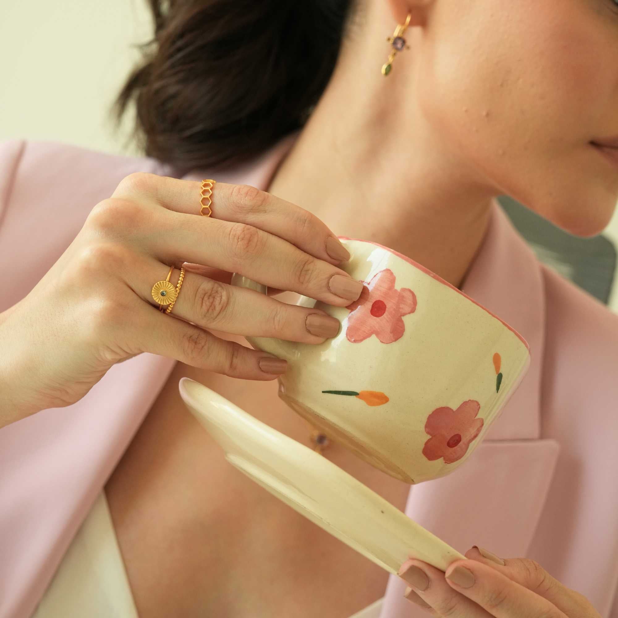Lifestyle portrait of a model holding a floral teacup and saucer, wearing a chic pink blazer and gold jewelry accents including the Delicate Vintage Beaded Stacking Ring Gold on her ring finger, by Protsaah Zurich.