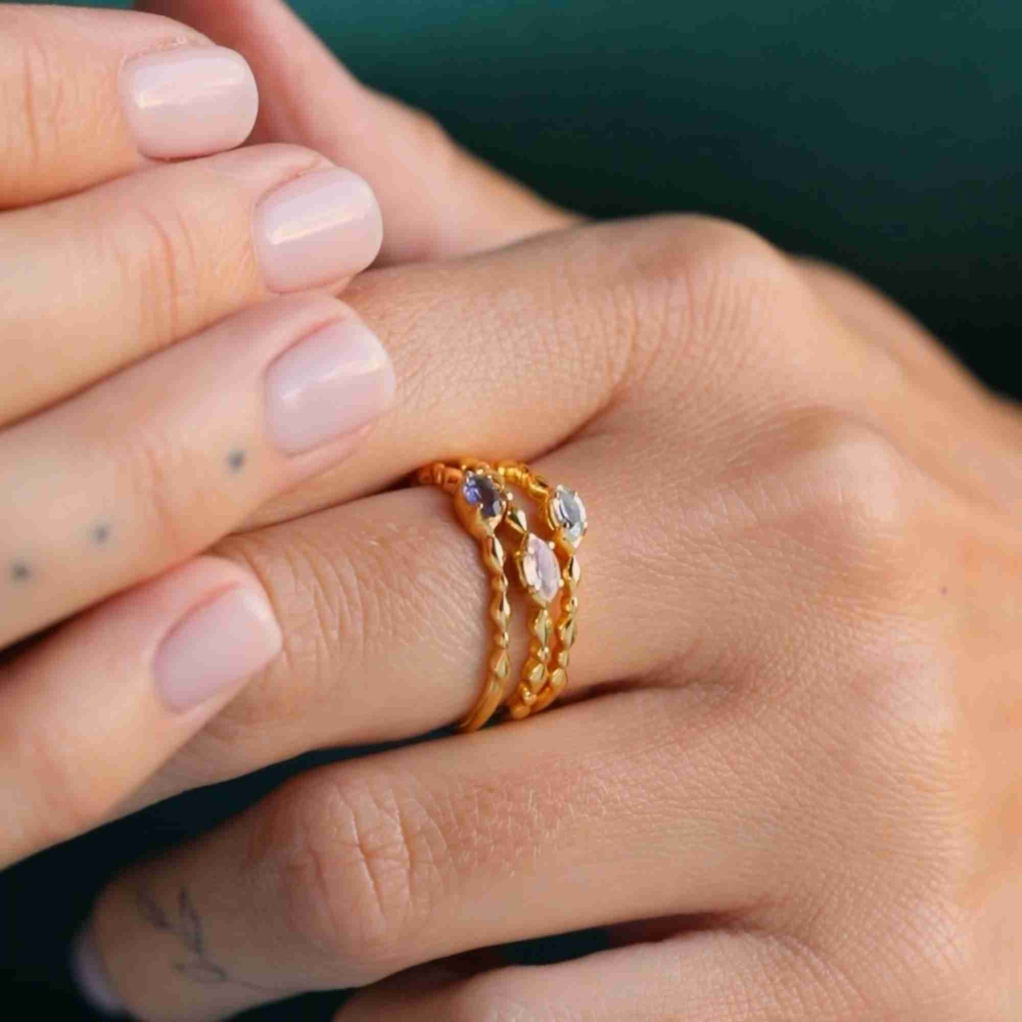 Side profile lifestyle picture named Delicate Vintage displaying a stack of three fine handmade 22K gold vermeil rings worn on a model's finger. The arrangement shows the delicate texture of the bubble bands and the subtle shimmer of the marquise-cut natural blue Topaz gemstone charm by Protsaah Zurich.