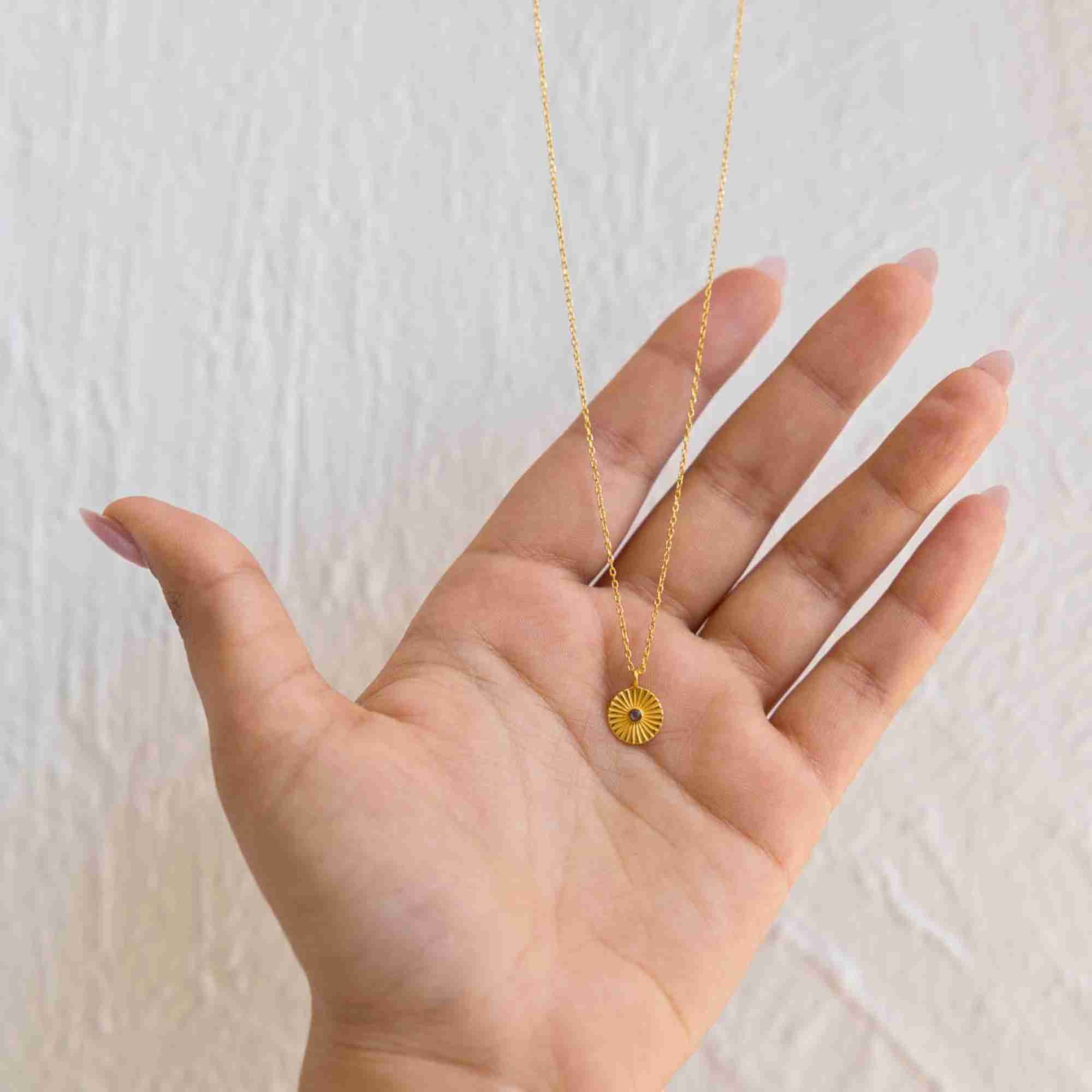Close-up view of the Delicate Vintage Labradorite Fluted Medallion Coin Pendant Necklace Gold resting in the palm of an open hand, referencing file name Delicate_Vintage_5.jpg. The shot illustrates the dainty scale of the fluted gold disk and the centered iridescent labradorite gemstone setting.