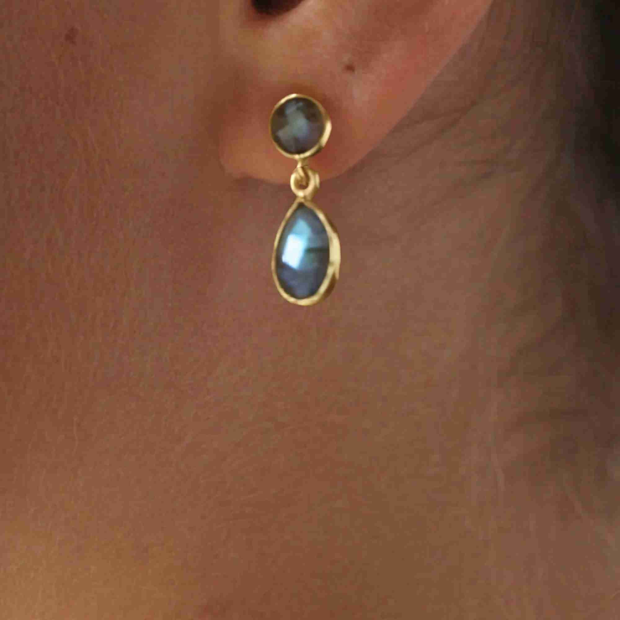 Close-up earshot model picture named Dew Drops displaying the Labradorite Stud & Teardrop Drop Earrings in gold vermeil, showcasing the beautiful play of light and signature blue-grey iridescent flash of the natural stones against the warm gold bezel setting when worn in natural light by Protsaah Zurich.