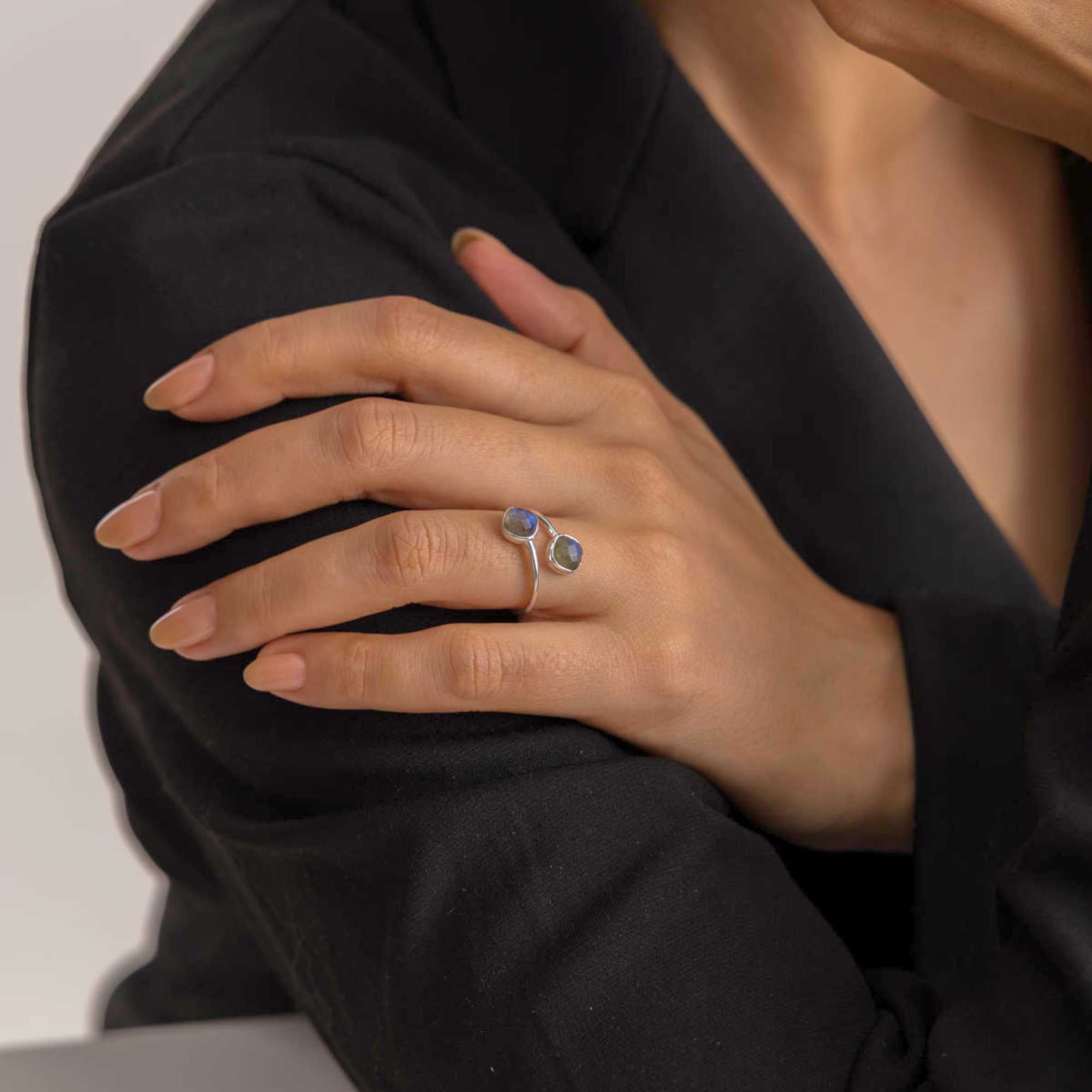 Slightly wider lifestyle portrait of a model in a black blazer, showcasing the Geo Glam Toi et Moi Labradorite Ring Gold, referencing file name 53.jpg. Her hand rests elegantly on her upper arm, displaying the open-shank bypass design of the ring and its two shimmering labradorite stones.