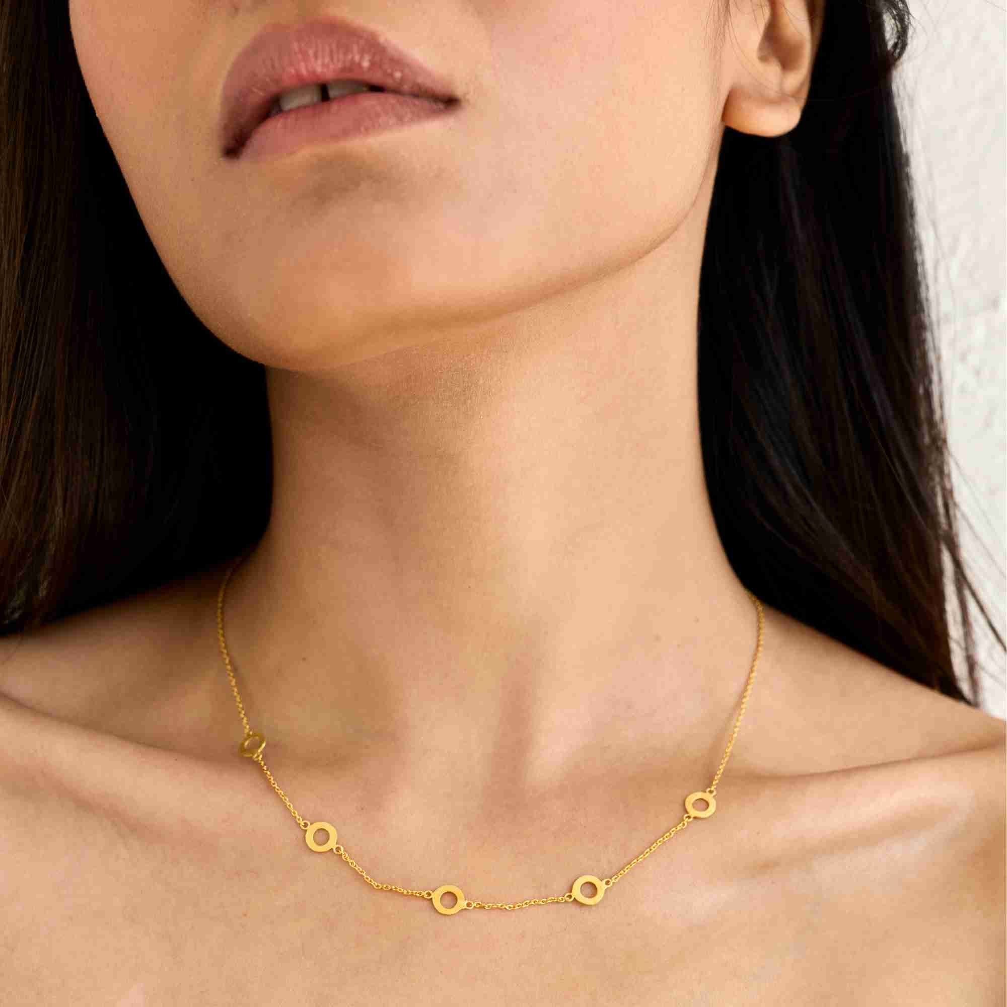 Model in an olive green top wearing the delicate gold Shimmering Disks Open Circles Choker Necklace resting along her collarbone.