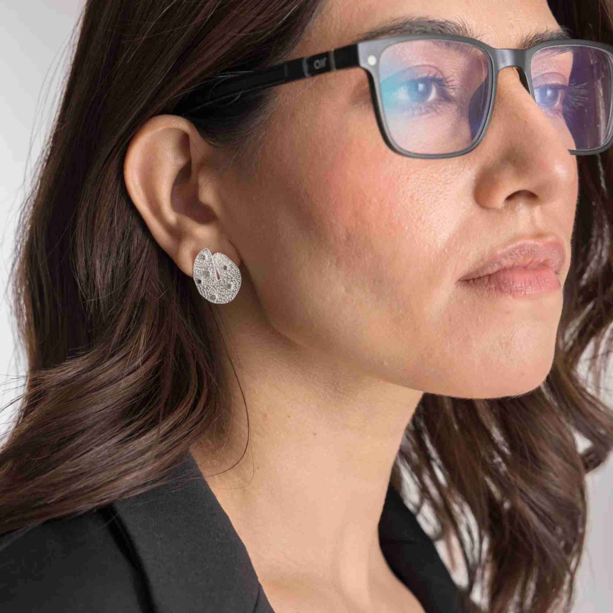 Softly lit studio lifestyle view of the Ribbons and Lace Galaxy Multi-Gemstone Stud Earrings Silver on a model, referencing file name Ribbon_Lace_18_b2d6ce7c-22f4-4395-b0c6-227edf1ec822.jpg. The model looks off-camera, allowing the intricate textured finish and scattered galaxy-inspired gemstones of the 92.5 sterling silver earring to catch the light.