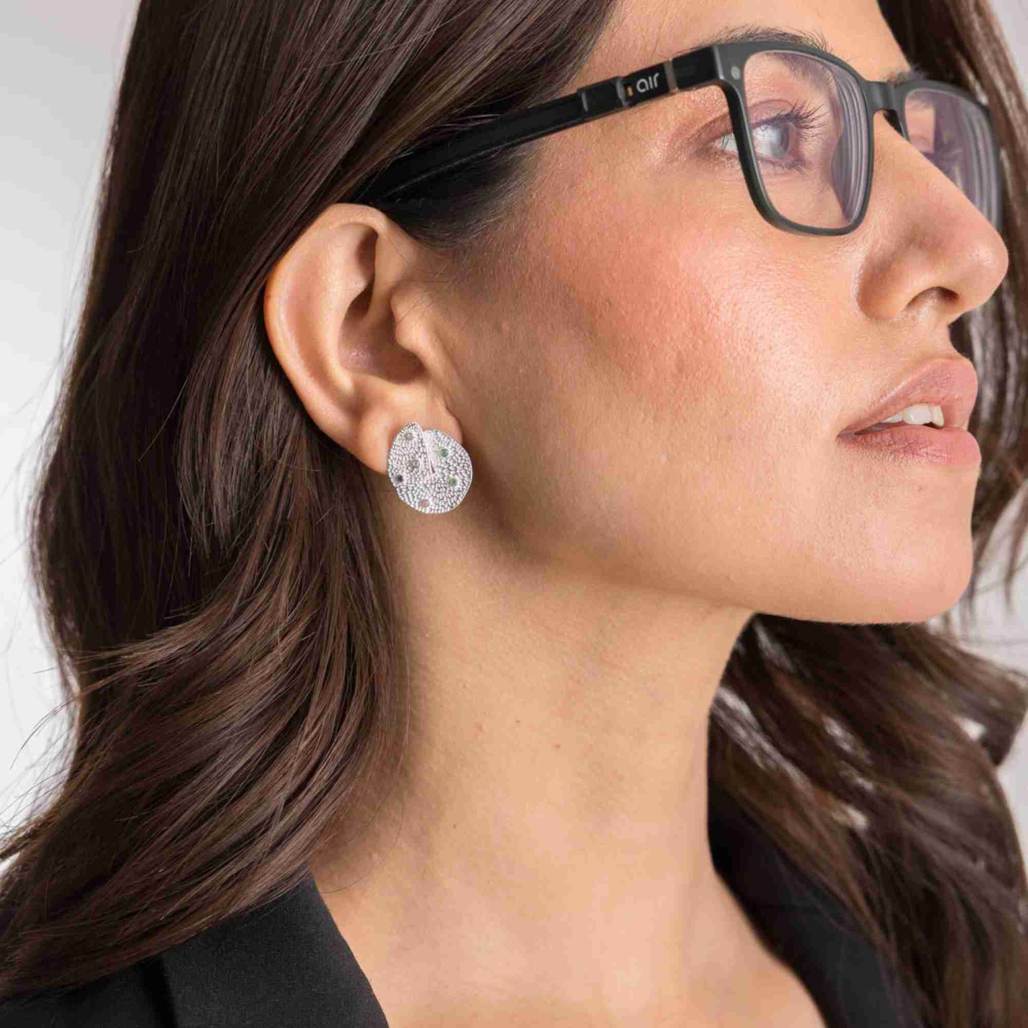Three-quarter lifestyle view of a model accessorized with the Ribbons and Lace Galaxy Multi-Gemstone Stud Earrings Silver, referencing file name Ribbon_Lace_19.jpg. The portrait focuses on the side profile of her face, accentuating the fine craftsmanship, abstract curved detailing, and embedded colorful gems on the silver statement stud earring.