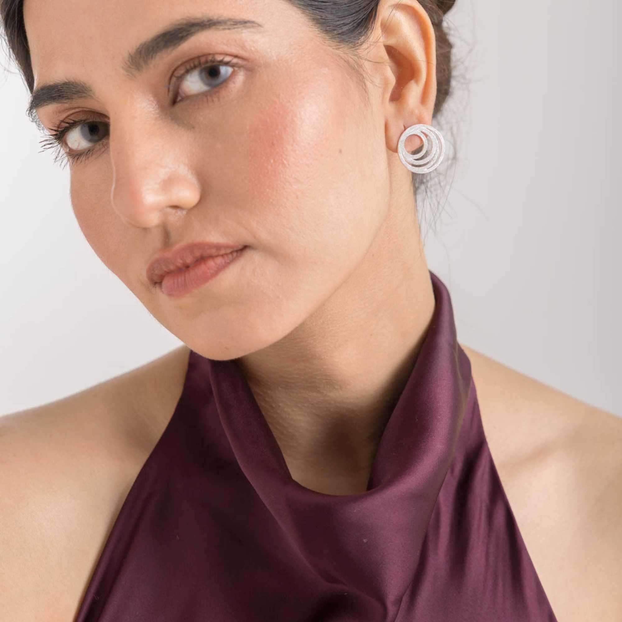 Up-close lifestyle view focusing on the side profile of the Shimmering Disks Intermingled Circles Stud Earrings Silver on a model, referencing file name 30_c9d89d81-44cf-43d5-98f9-6e2b15f0132b.jpg. The image provides a clear look at how the large, open-cut concentric circle statement stud sits flat against the earlobe, highlighting its modern minimalist craftsmanship.