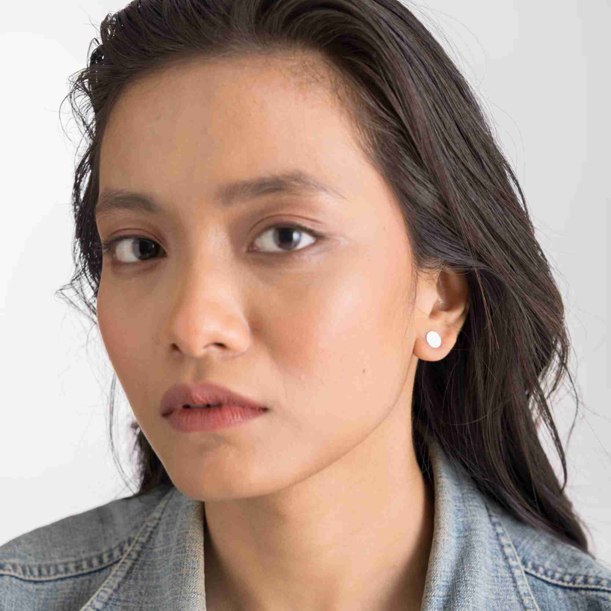 Front-facing lifestyle portrait of a woman wearing the Shimmering Disks Minimalist Stud Earrings Silver, referencing file name Shimmering_Disks_71_424b2373-e328-4892-b34c-3fd8286966cd.jpg. The composition shows the model looking directly into the camera, illustrating how these dainty, geometric silver coin studs offer a clean and subtle accent for everyday wear.